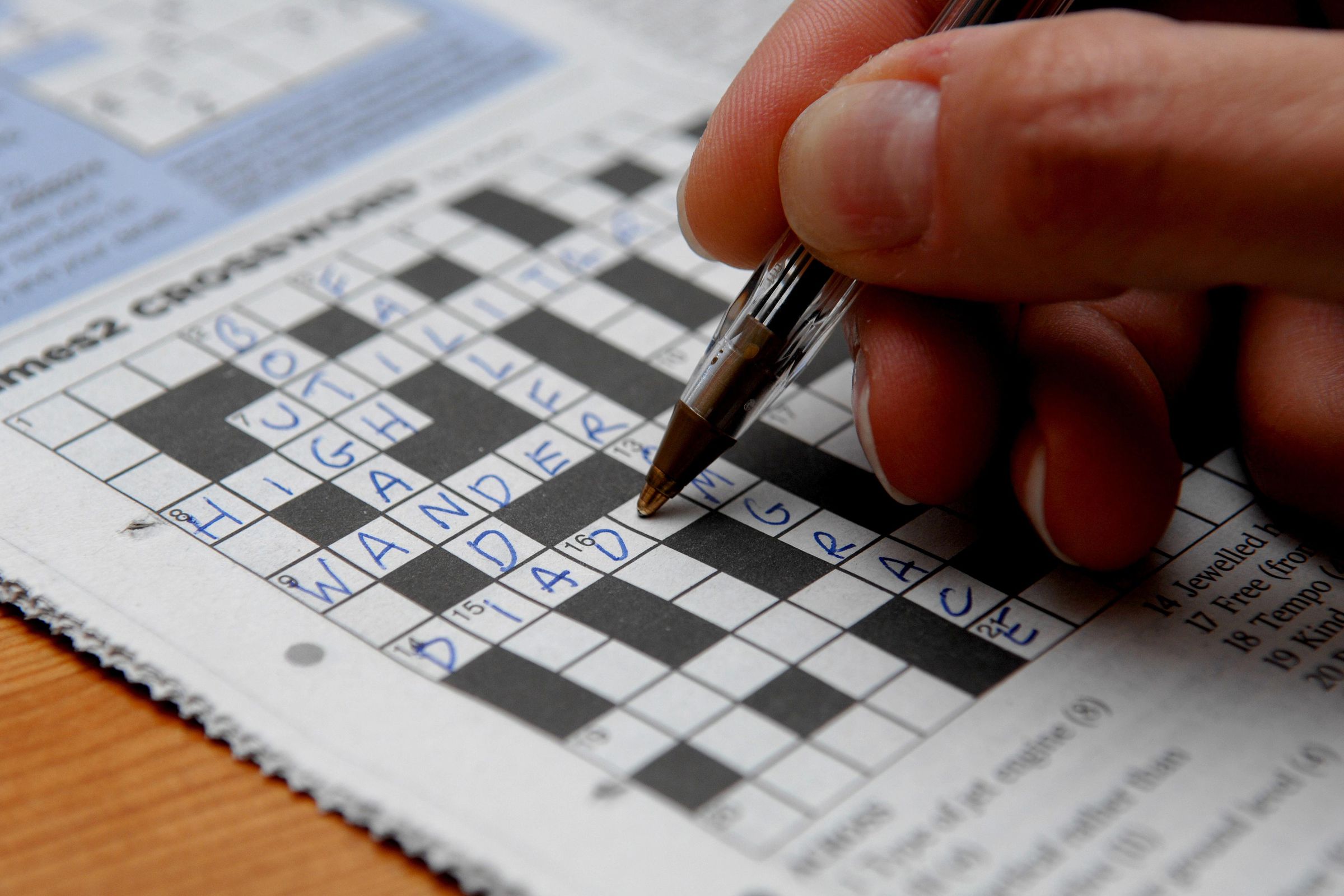 Photo of a crossword puzzle being completed by a hand holding a pen. 