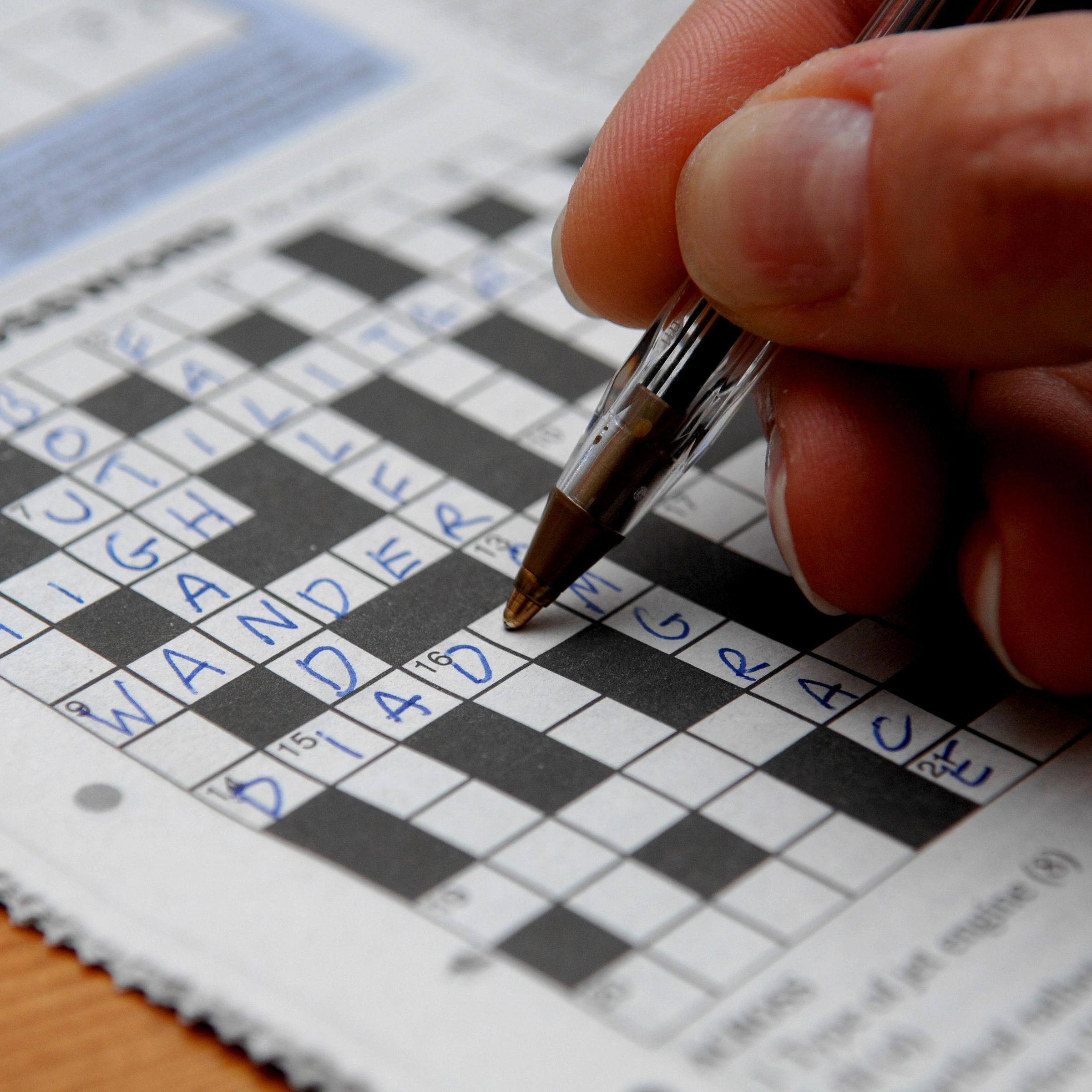 Photo of a crossword puzzle being completed by a hand holding a pen. 