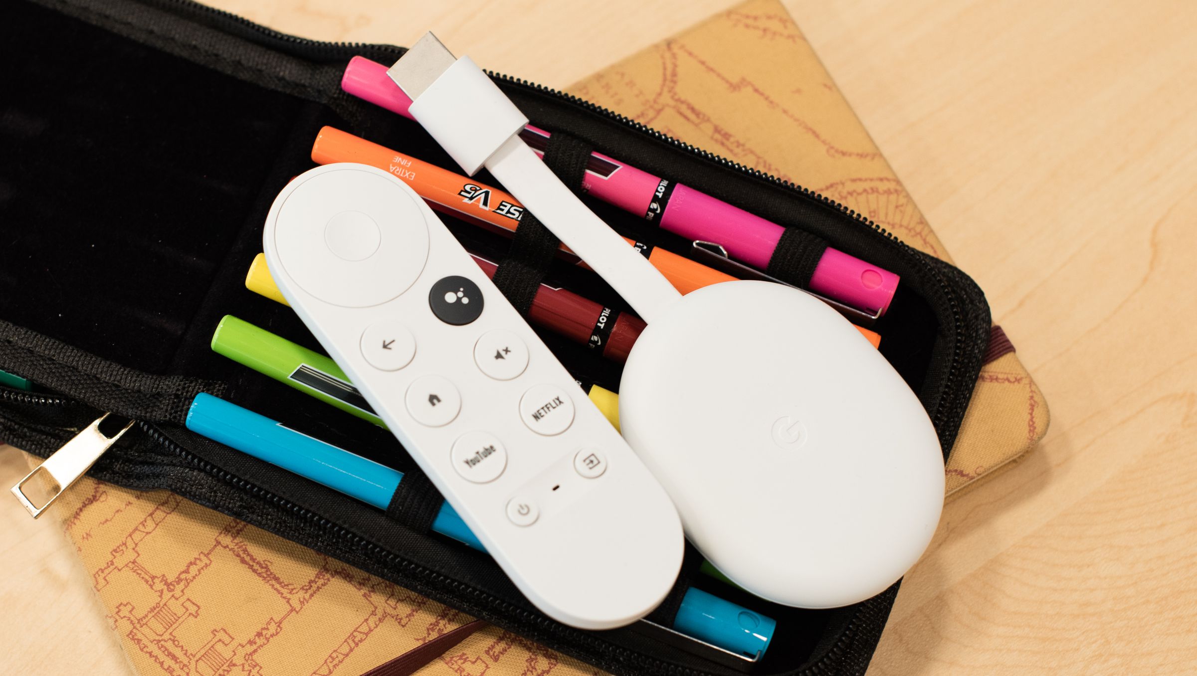 Image of a Chromecast with Google TV sitting on a bag of pens. It’s a white, oval-shaped device, with an HDMI cable sticking out from the front.