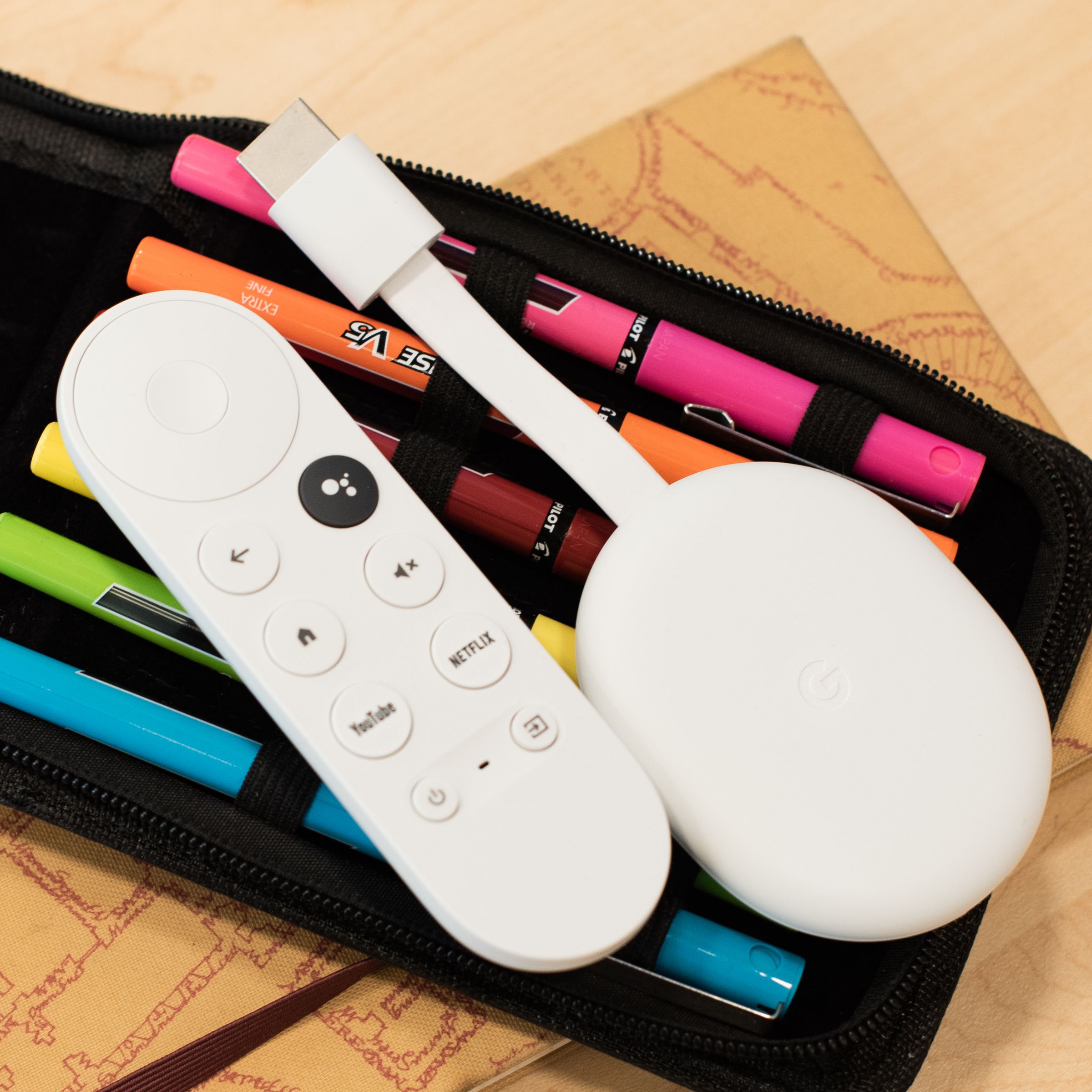 Image of a Chromecast with Google TV sitting on a bag of pens. It’s a white oval-shaped device with an HDMI cable sticking out from the front.