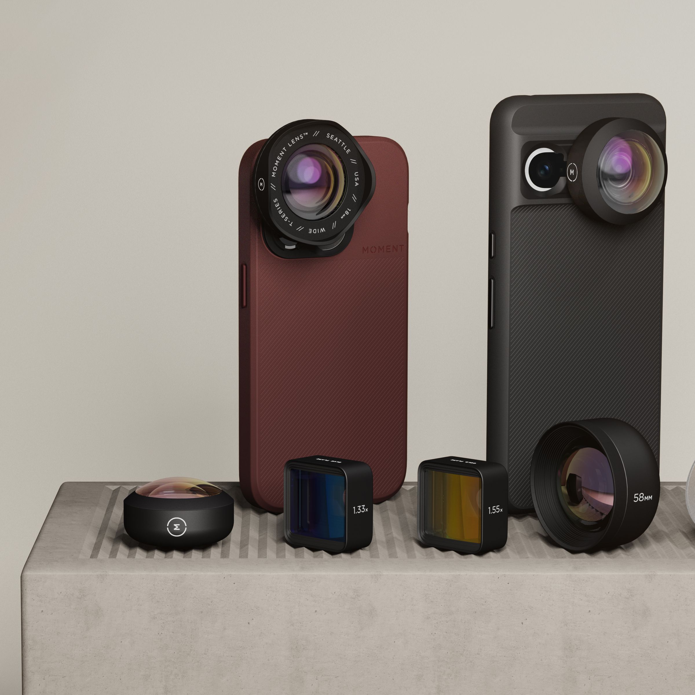 A picture of two smartphones — an iPhone on the left and a Pixel 7 on the right — with Moment cases and lenses attached. In front of them, other Moment lenses are lined up.