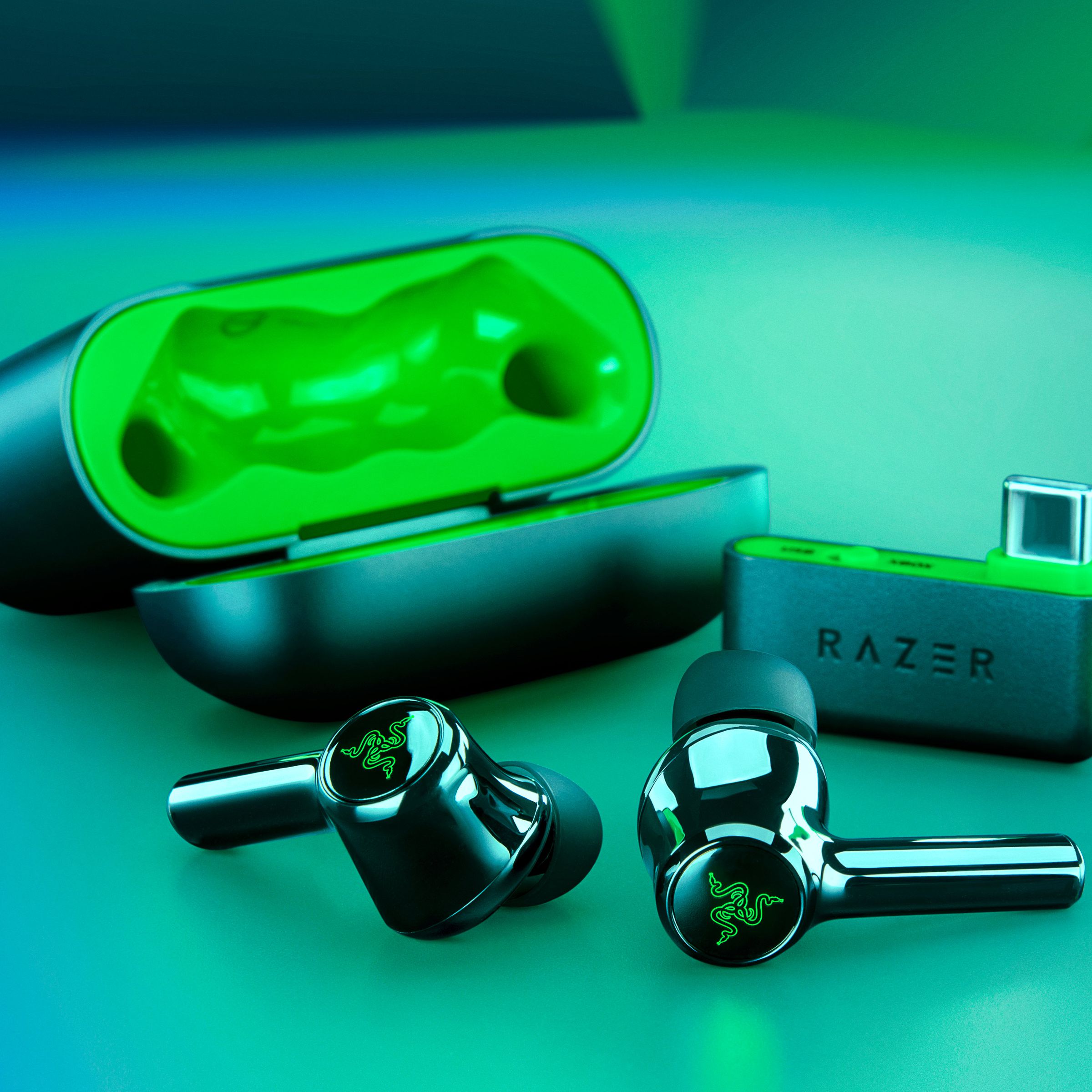 Razer’s Hammerhead HyperSpeed wireless earbuds sitting outside of their charging case next to the included USB-C audio transmitter.