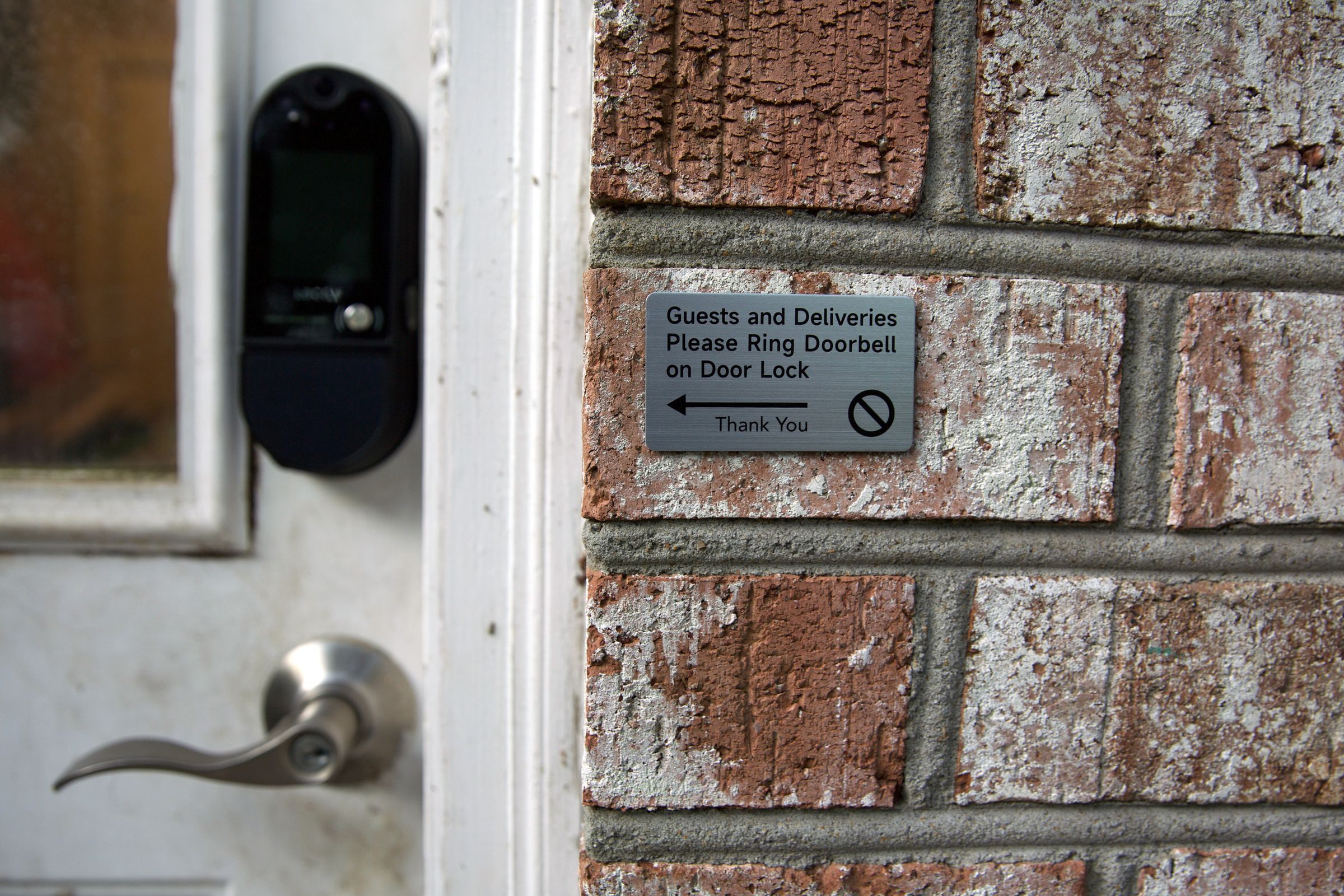 An image of a sign reading “Guests and Deliveries Please Ring Doorbell on Door Lock,” with an arrow pointing towards the Lockly Vision Elite installed in a door.