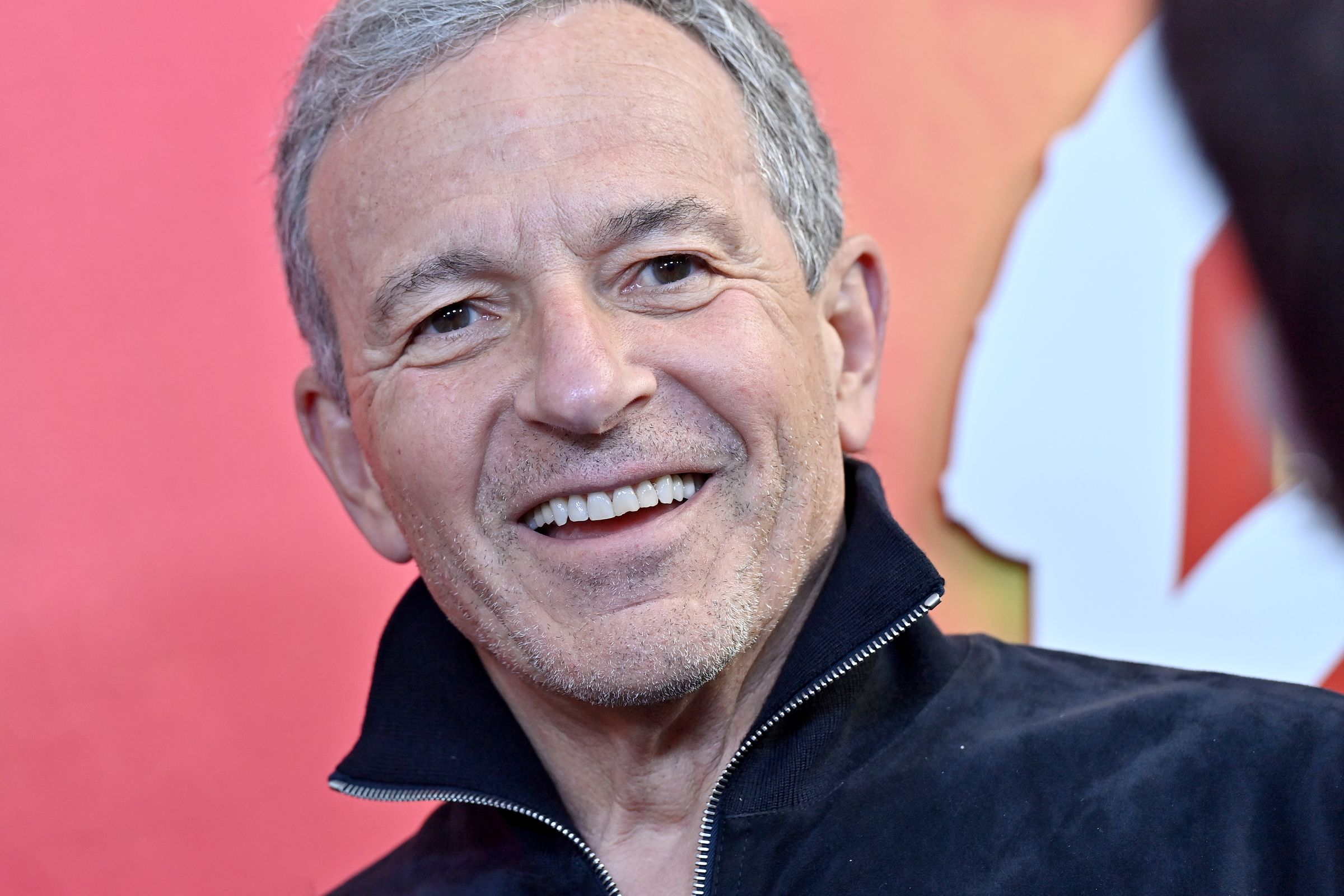 Disney CEO Bob Iger, an older white man with graying hair and wearing in a black sweater zip up, smiles at the camera.
