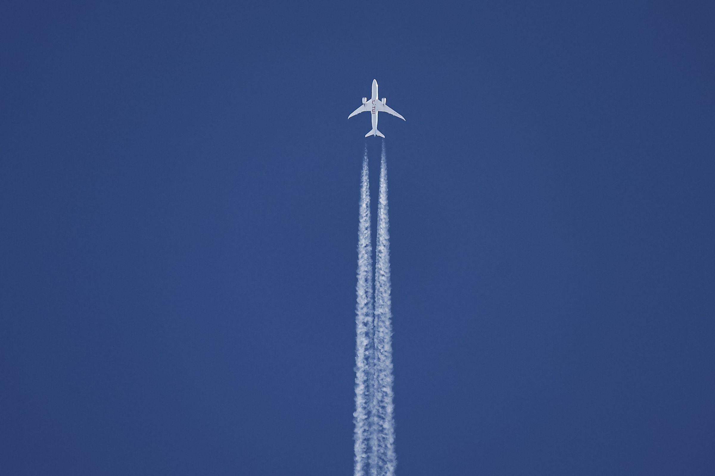 A plane flying against a blue sky with contrails behind it.