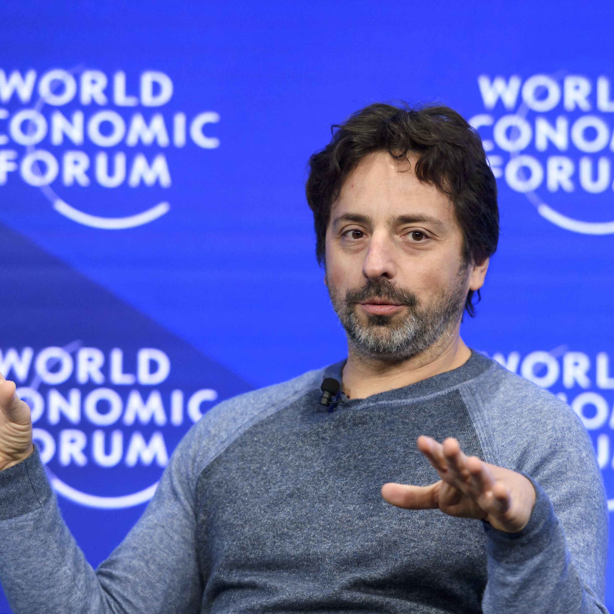 A picture of Sergey Brin holding his hands up mid-gesture while speaking at the World Economic Forum.