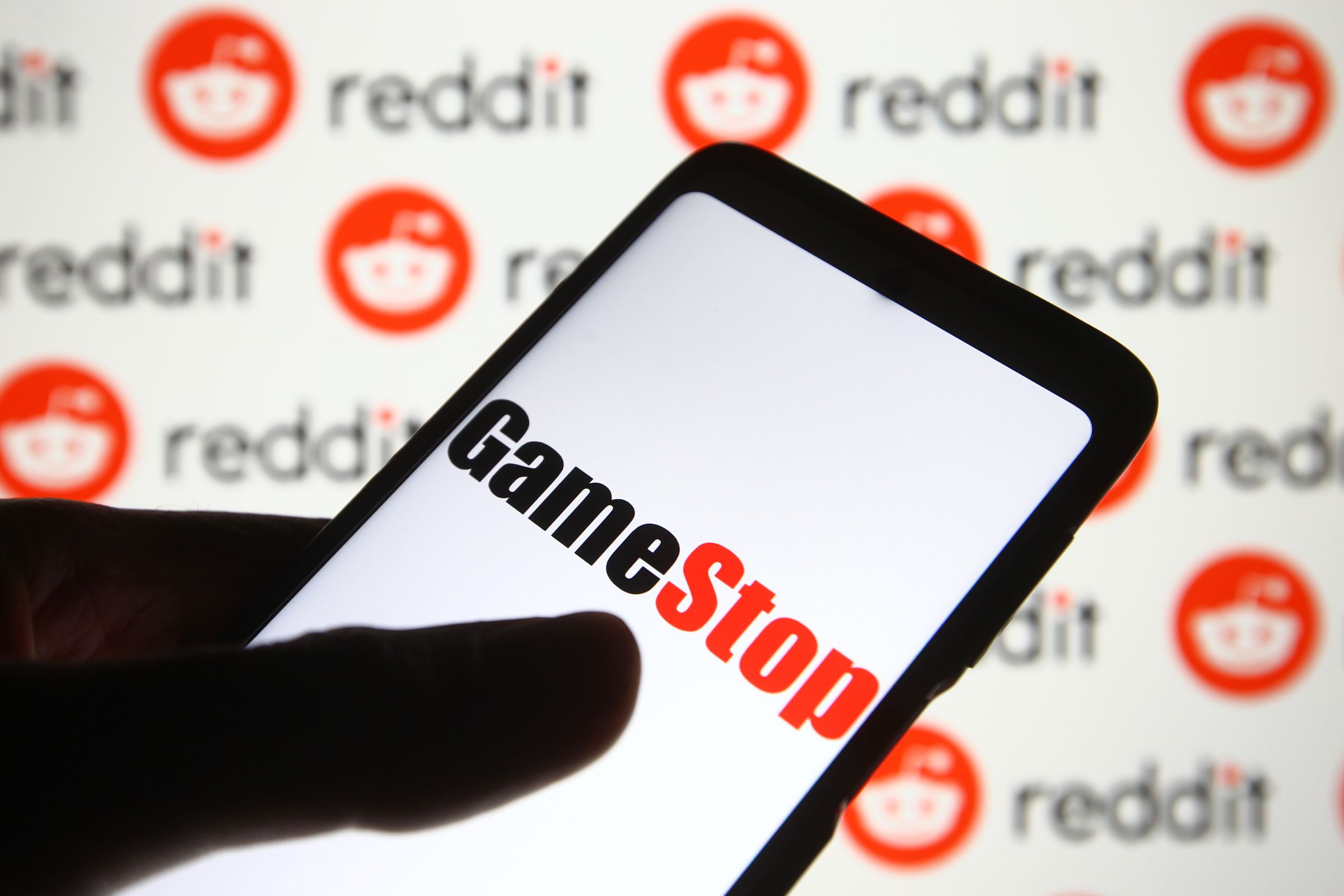 In this photo illustration a GameStop logo is seen on a mobile phone screen in front of Reddit logo.