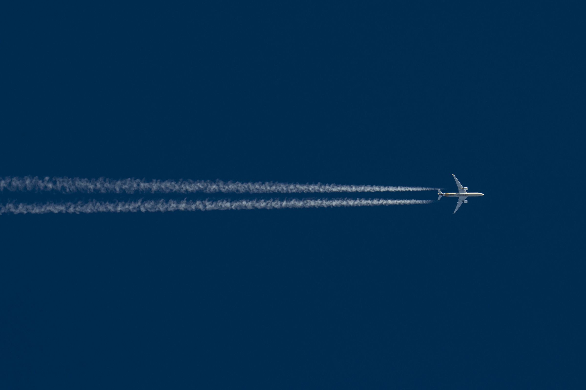 A plane flying across a blue sky with contrails behind it.