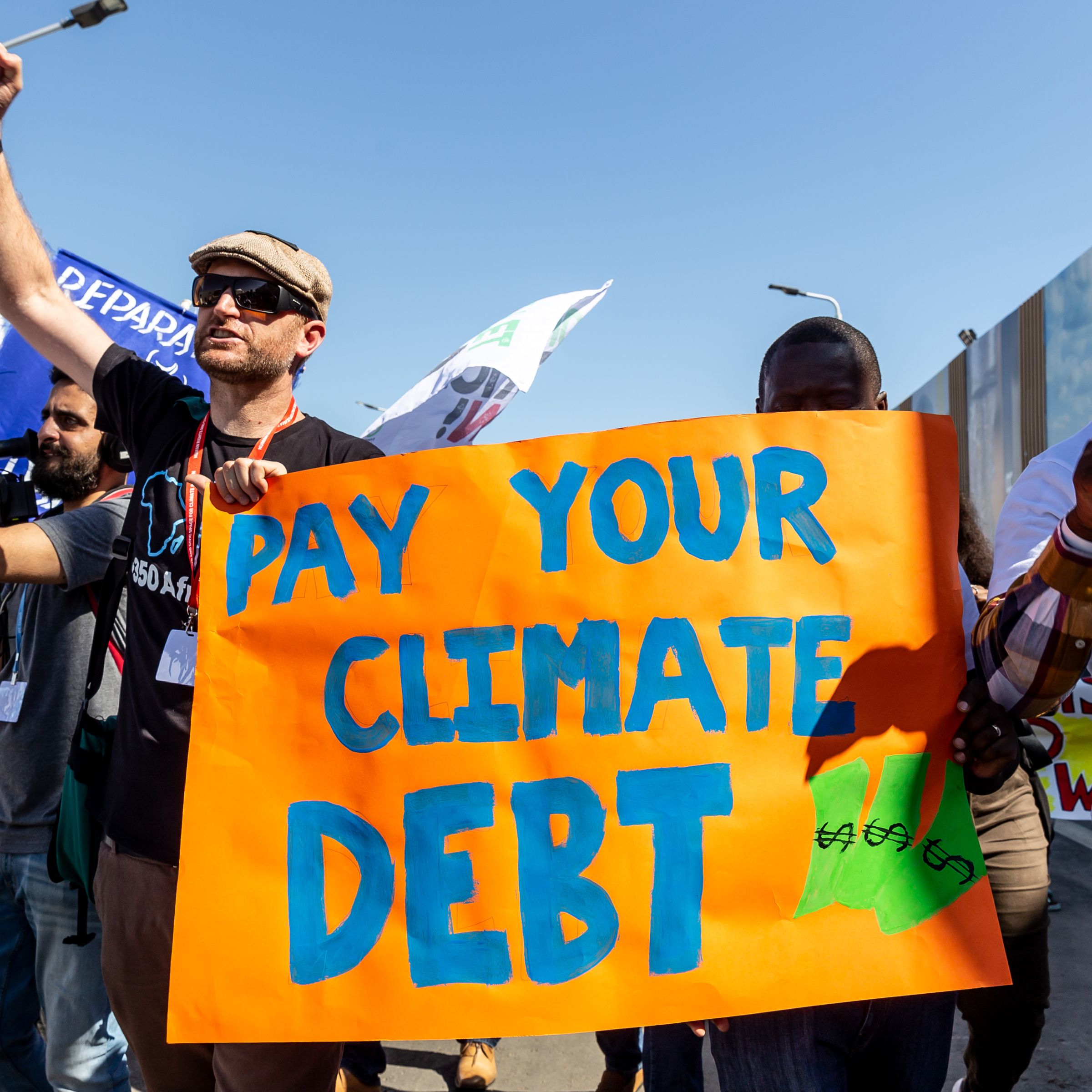 Protesters carry a sign that says “Pay your climate debt.”