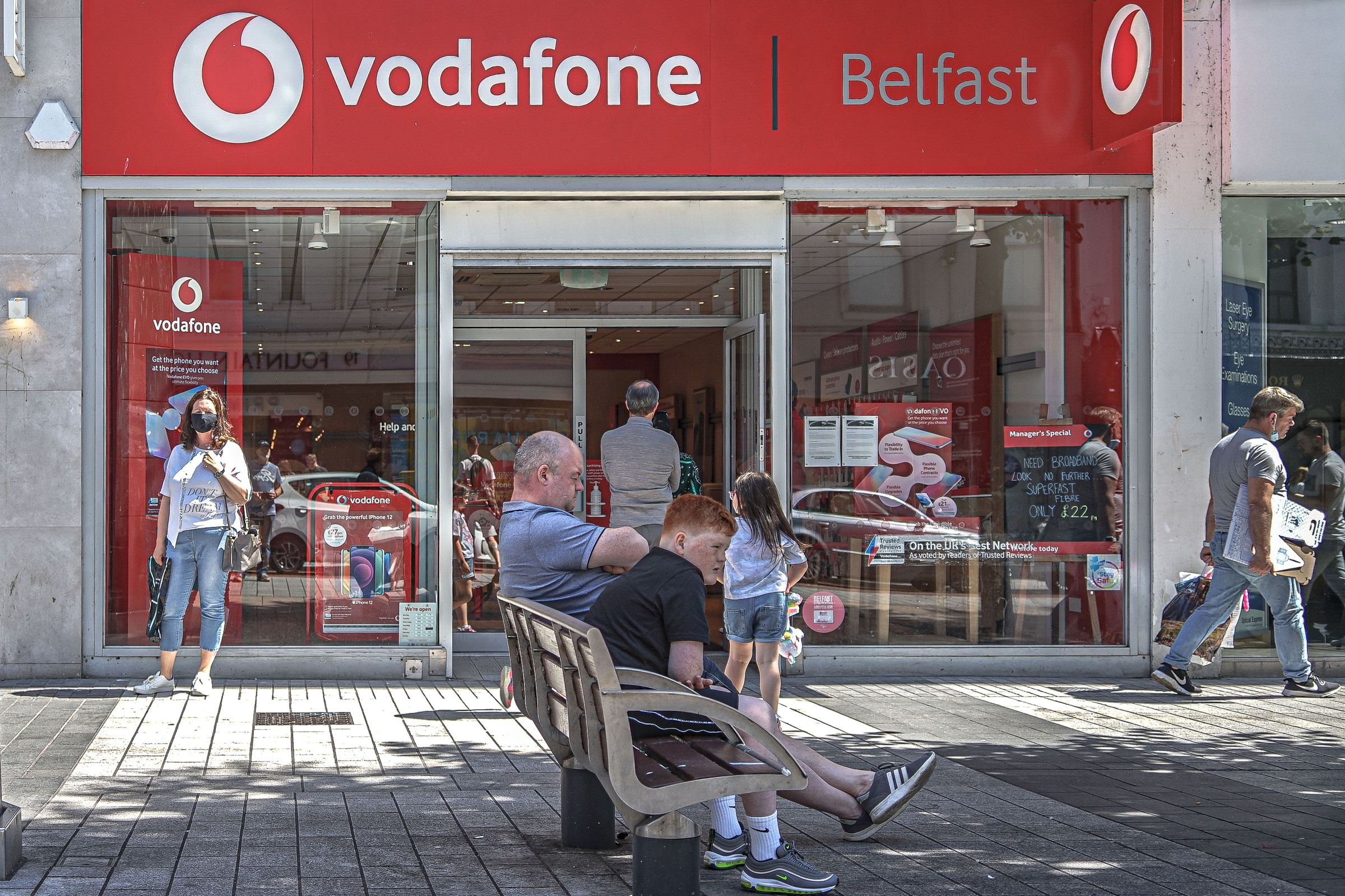 Masked customers queue to enter Vodafone Mobile Phone Store...