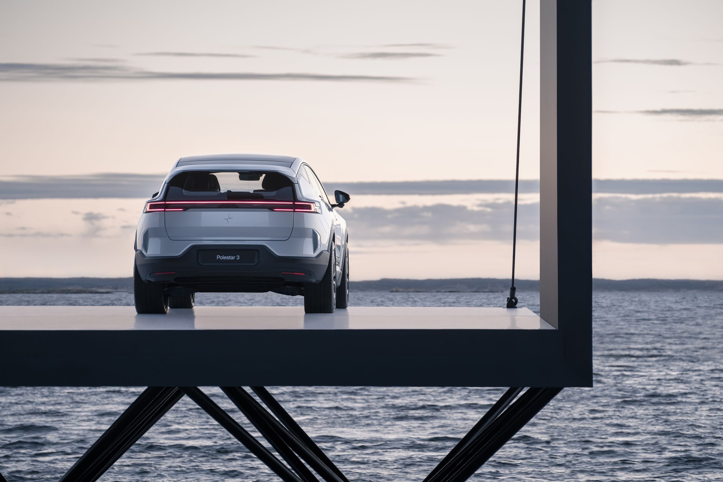 The Polestar 3 electric SUV seen from the rear parked on a pier overlooking the sea. 