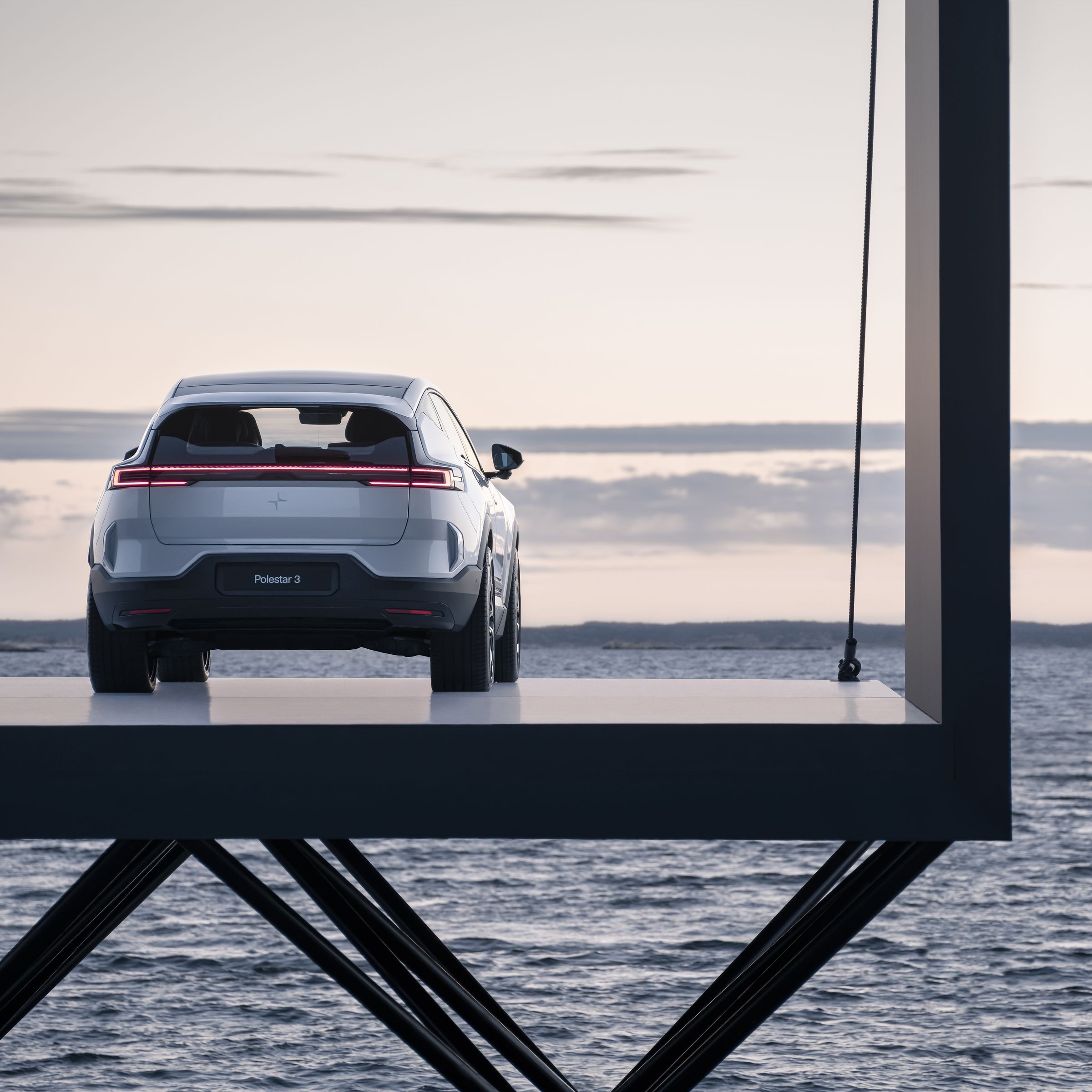 The Polestar 3 electric SUV seen from the rear parked on a pier overlooking the sea. 