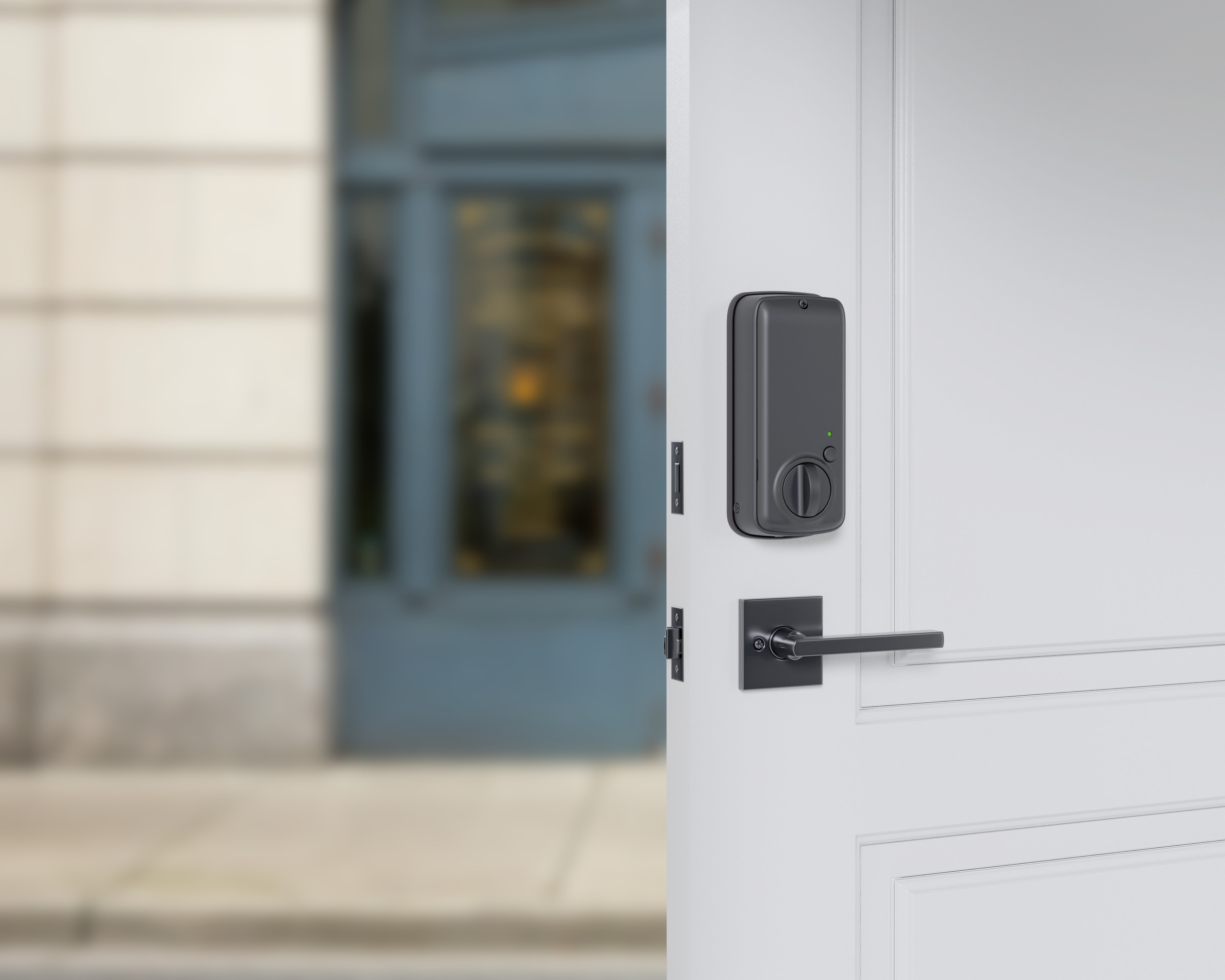 The interior portion of a smart deadlock, in black, on a white door. A street scene is blurred in the background.
