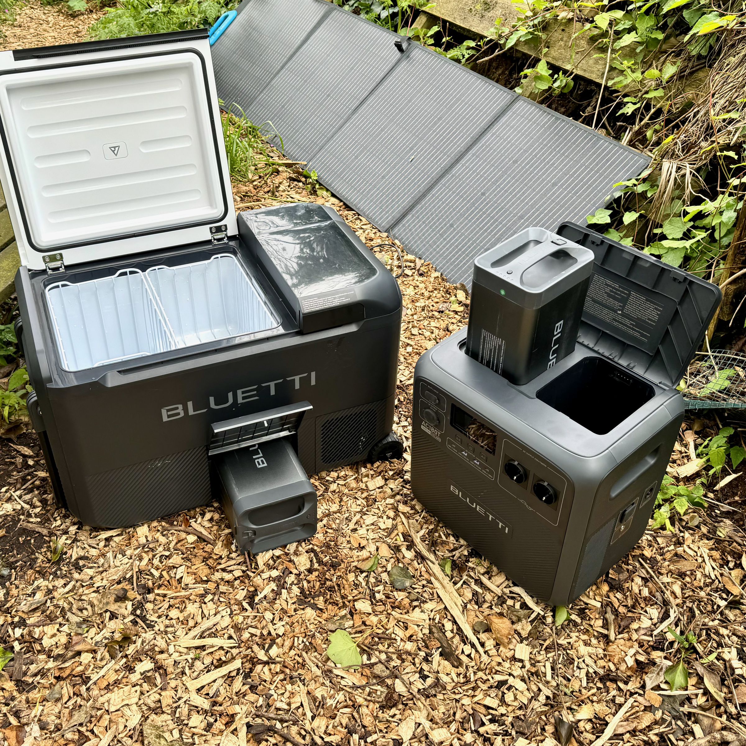 The Bluetti MultiCooler and AC180T solar generator sitting in a park next to a picnic table with a solar panel in the background.