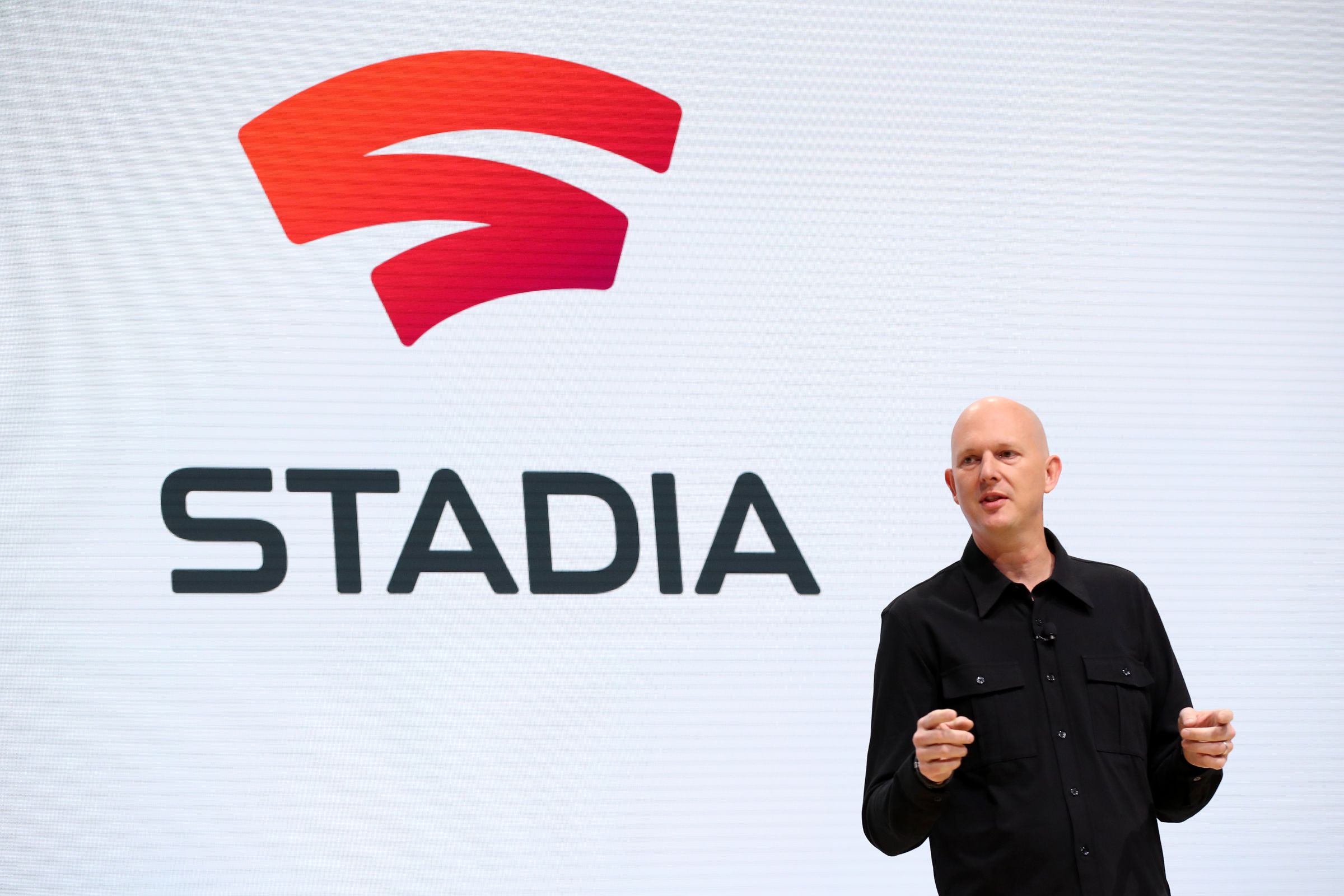 Google’s Phil Harrison is shown making an announcement onstage with a Stadia graphic behind him.