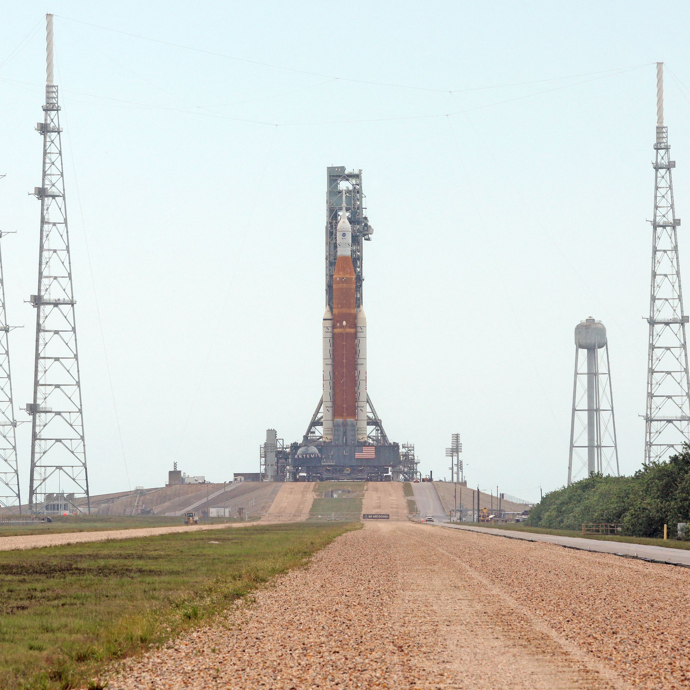 A rocket sits on the launchpad at the end of a dirt road.
