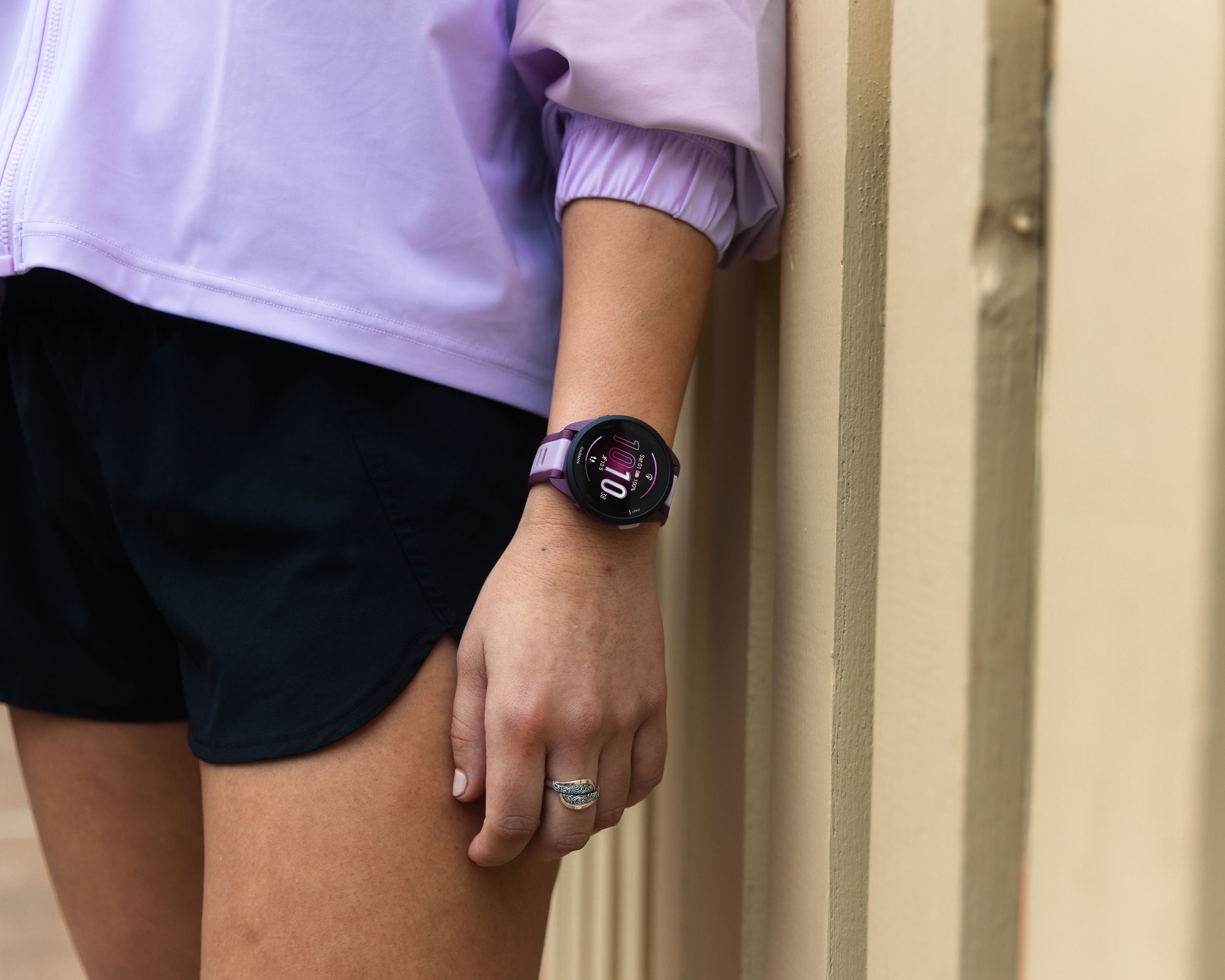Woman leaning on wall wearing purple Garmin Forerunner 165 watch