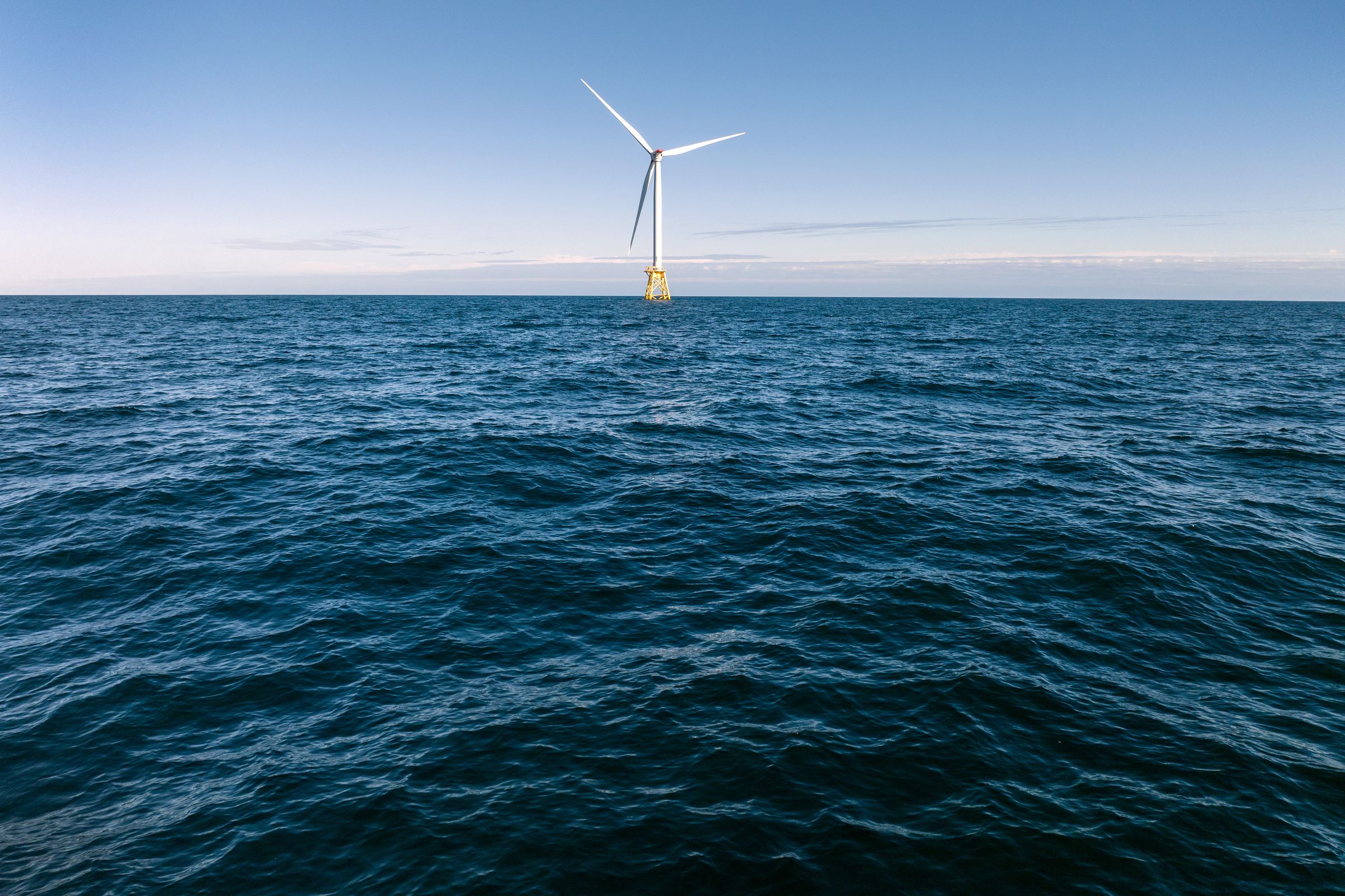 A single turbine standing in the ocean with the horizon behind it.