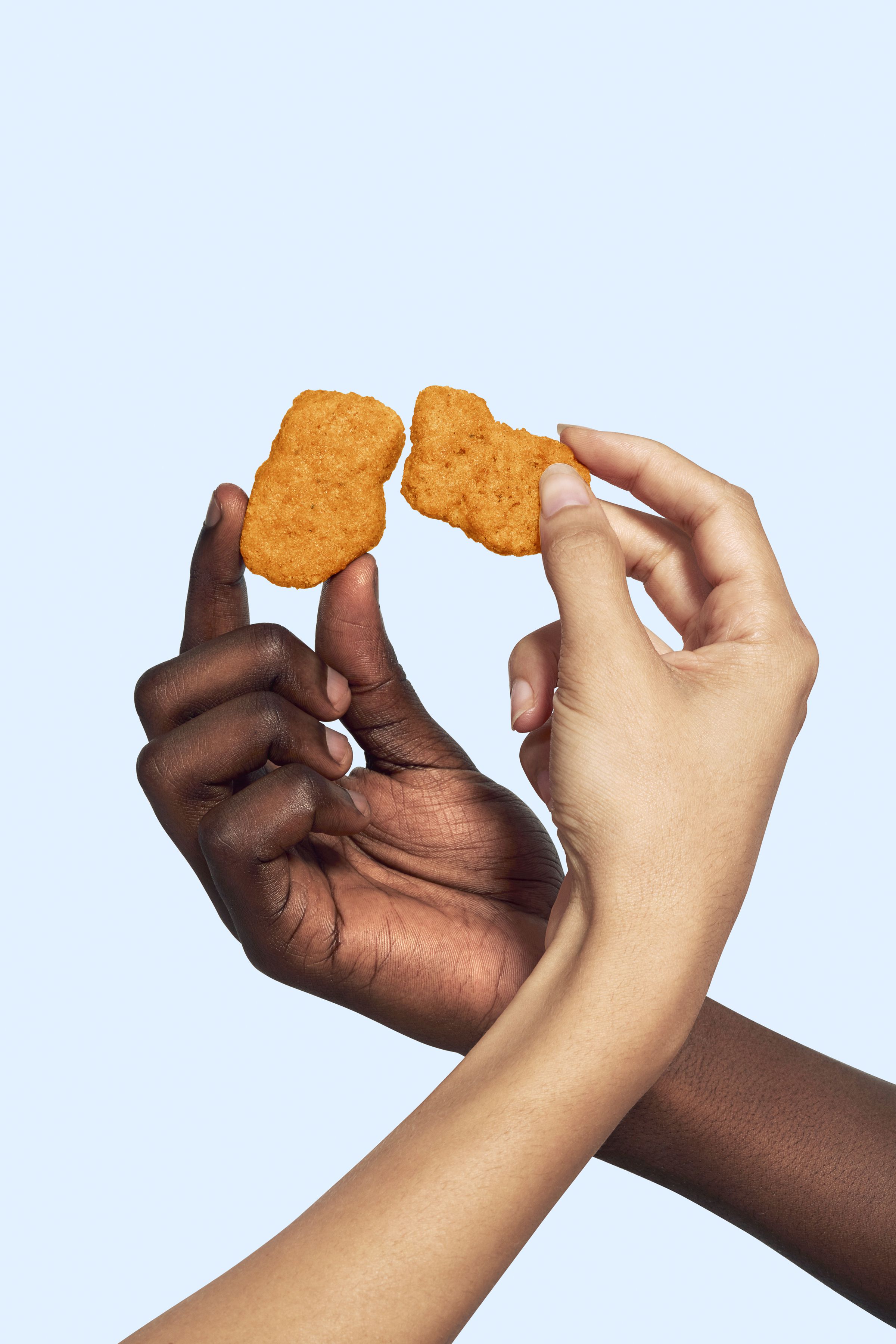 The hands of two people, crossed at the wrists, holding nuggets that are almost touching. 