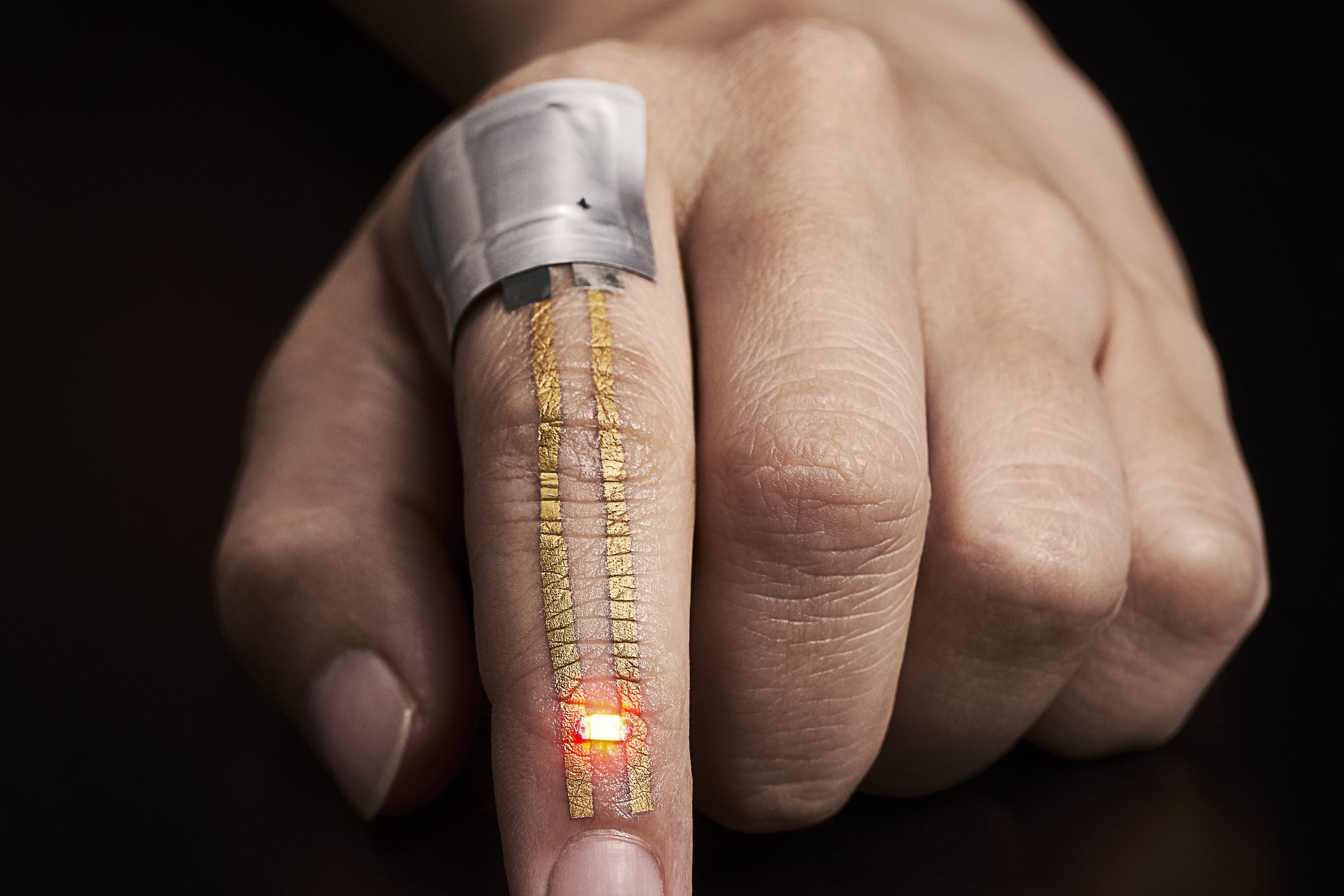 Index finger with gold nanomesh conductor. The electric current from a flexible battery placed near the knuckle flows through the conductor and powers the LED just below the fingernail. 
