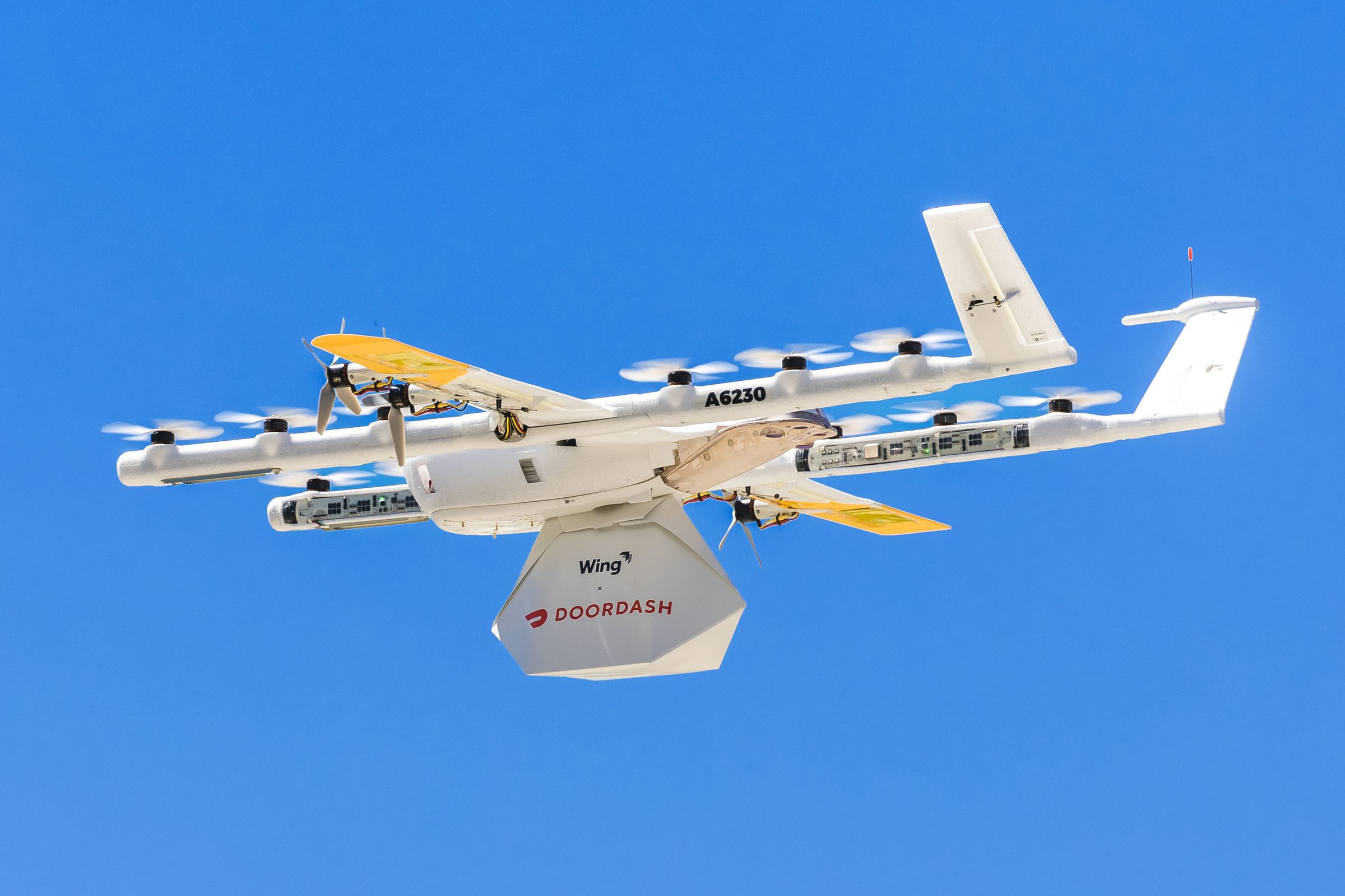 Image of a drone carrying a parcel marked with Wing and Doordash’s logos.