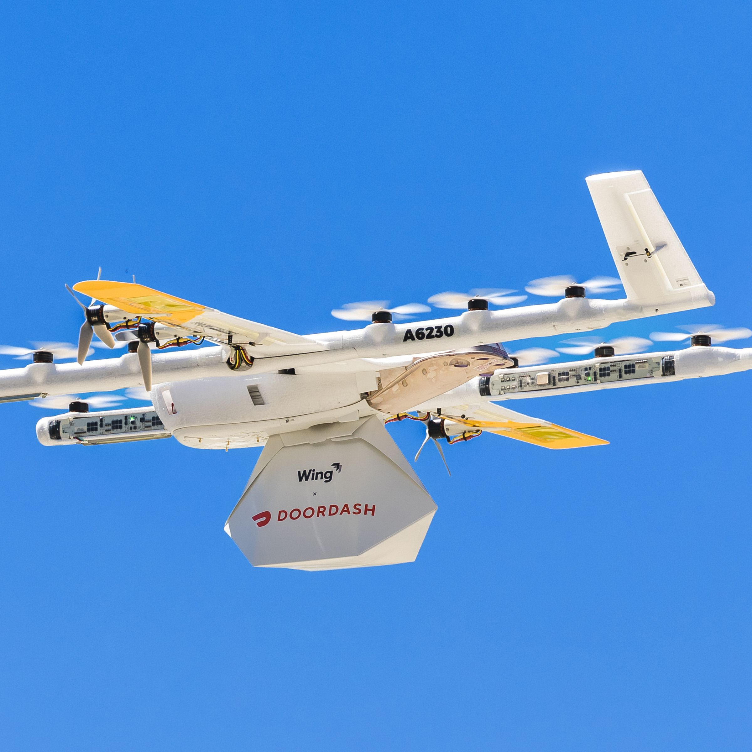 Image of a drone carrying a parcel marked with Wing and Doordash’s logos.