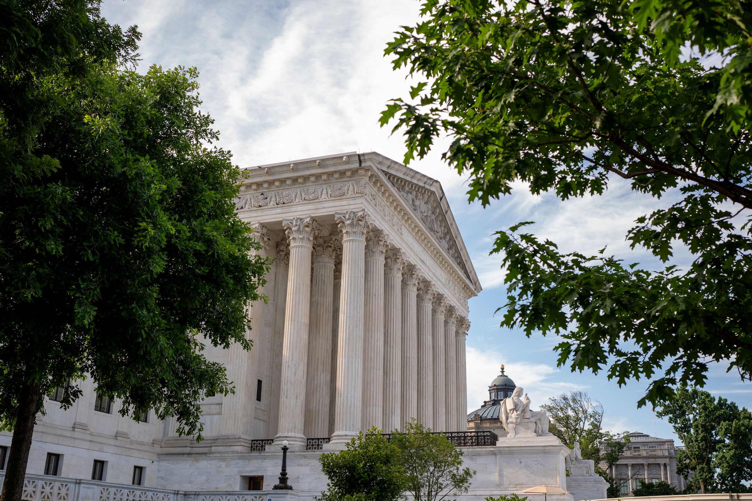 A view of the Supreme Court from the side, partly obstructed by tree foliage.