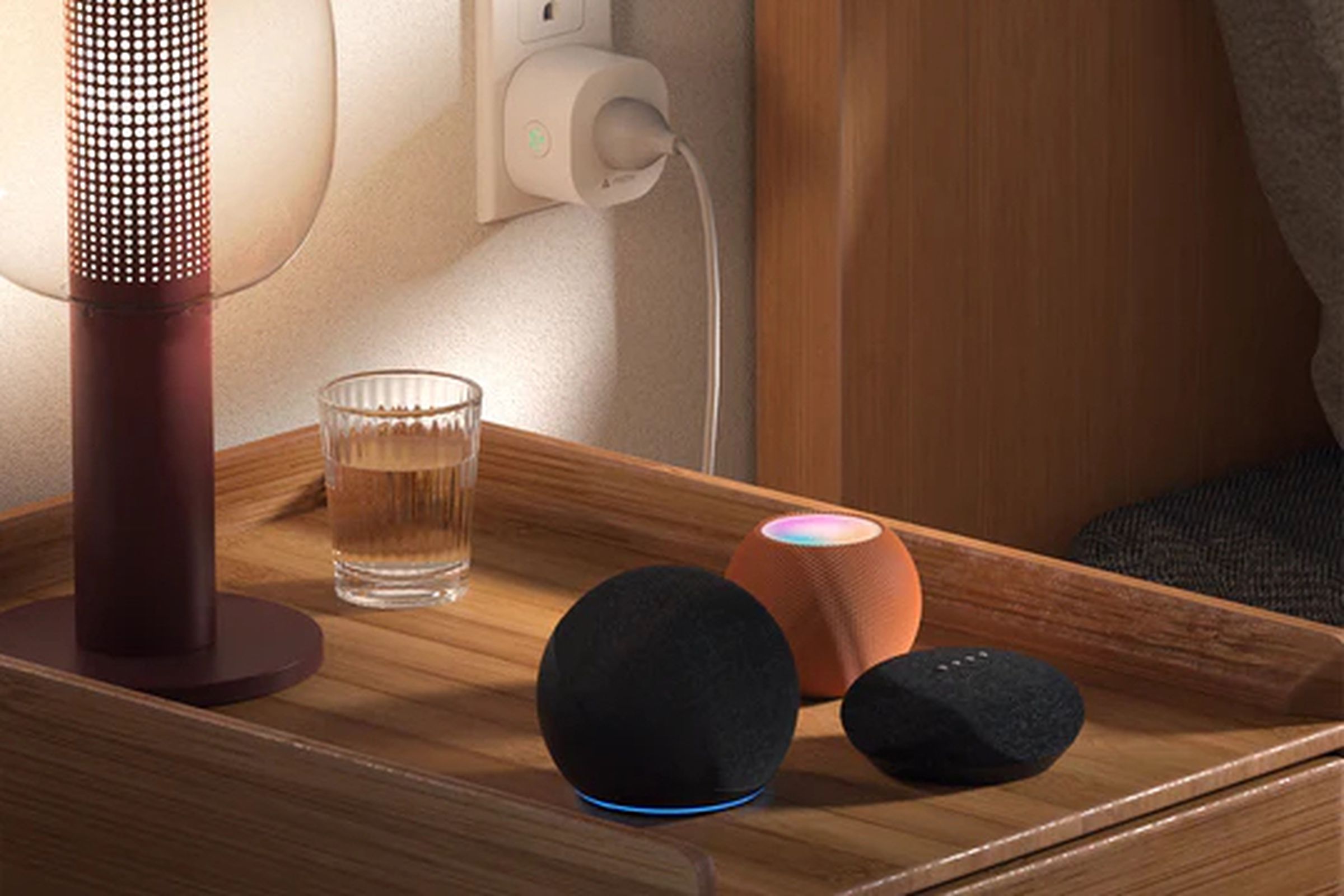 A lamp plugged into a smart plug next to three smart speakers.