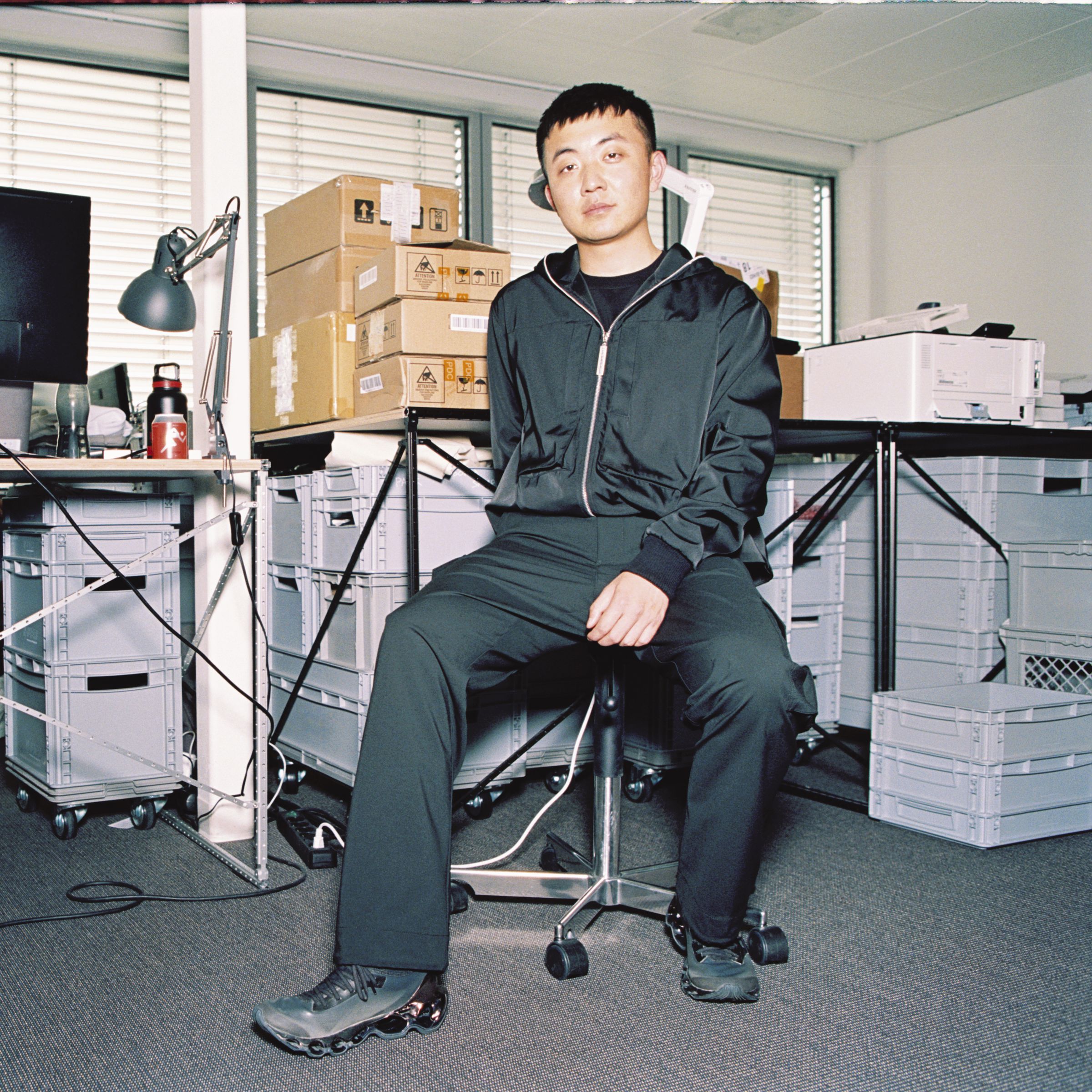 Nothing CEO Carl Pei in his office, surrounded by desks, computers, and cardboard boxes.