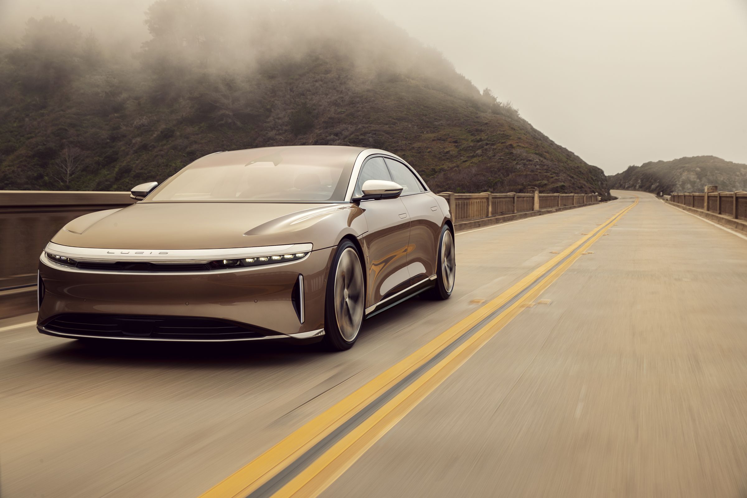 A picture of the Lucid Air driving on a two-lane road, pictured from the front in three-quarter view.