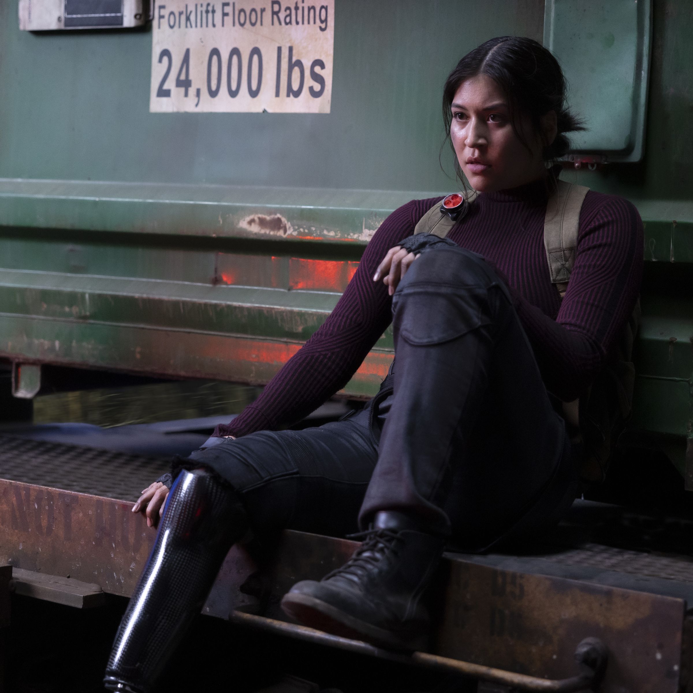 An image of Alaqua Cox as Maya Lopez. She’s dressed in combat gear and sitting on machinery looking exhausted after a fight.