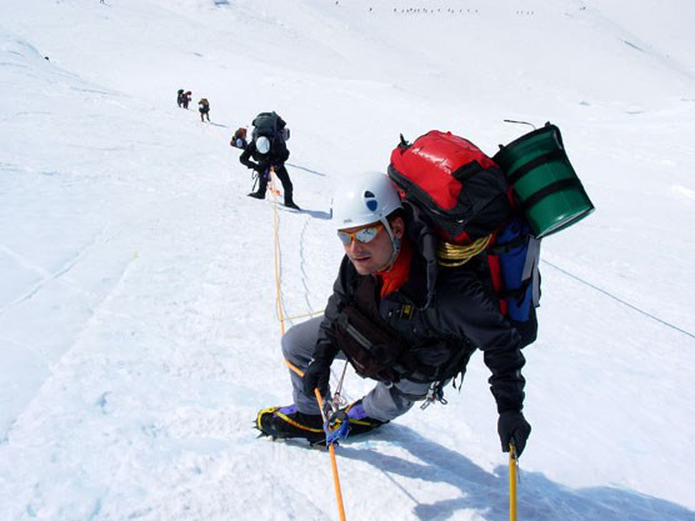 Climbers on Denali, with the green Clean Mountain Can attached to a backpack.