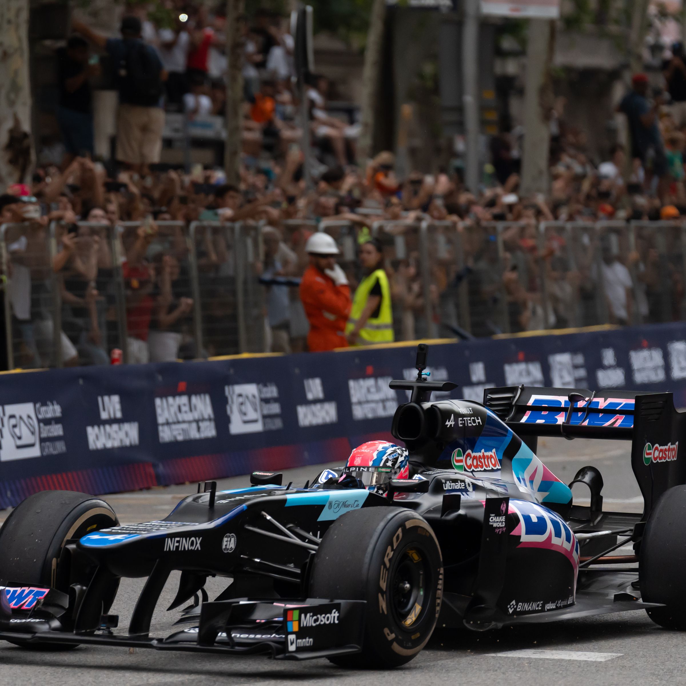 An F1 car driving on a track, with a crowd behind it.