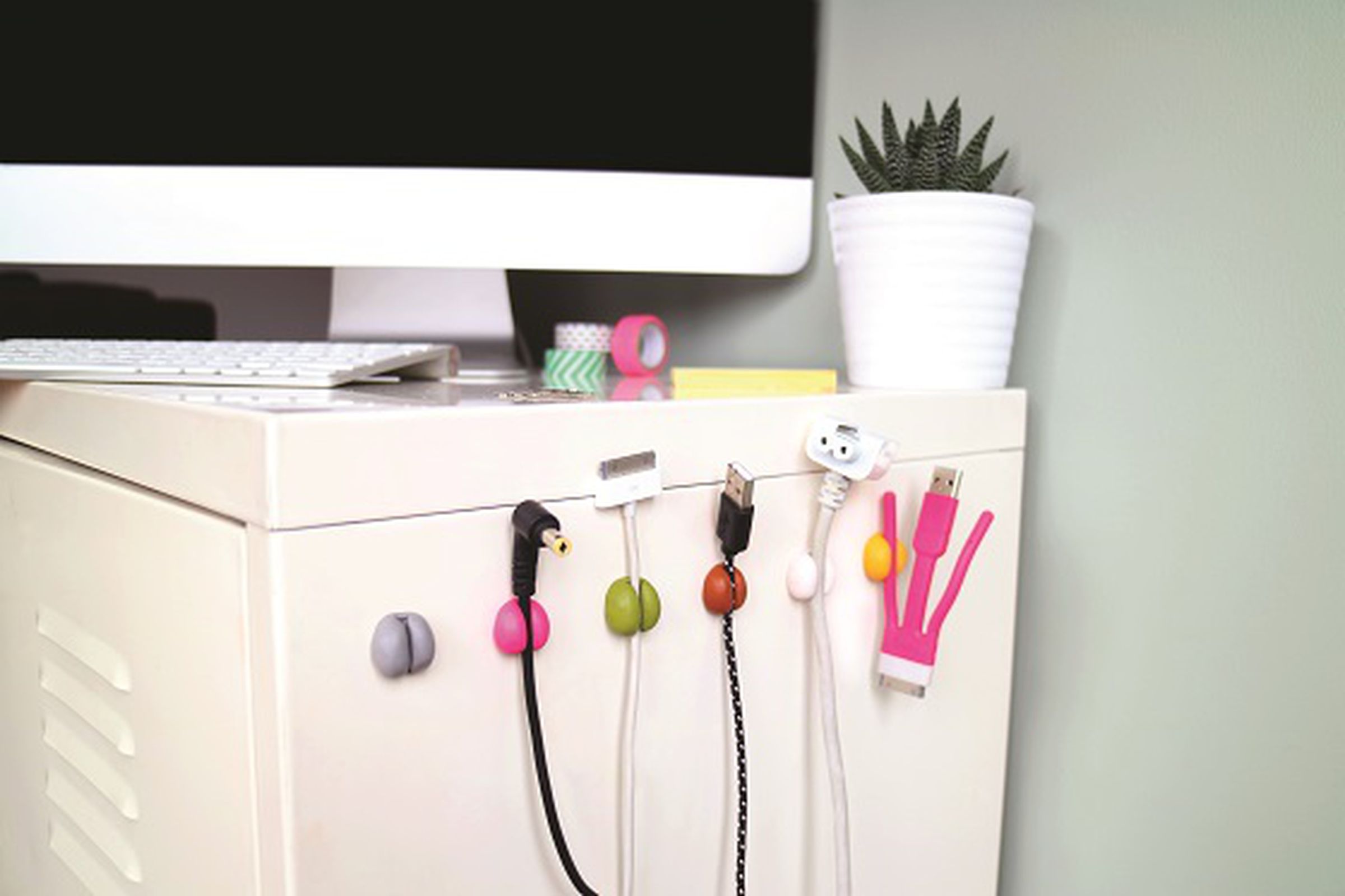 Round colorful cable holders stuck to the side of a desk.