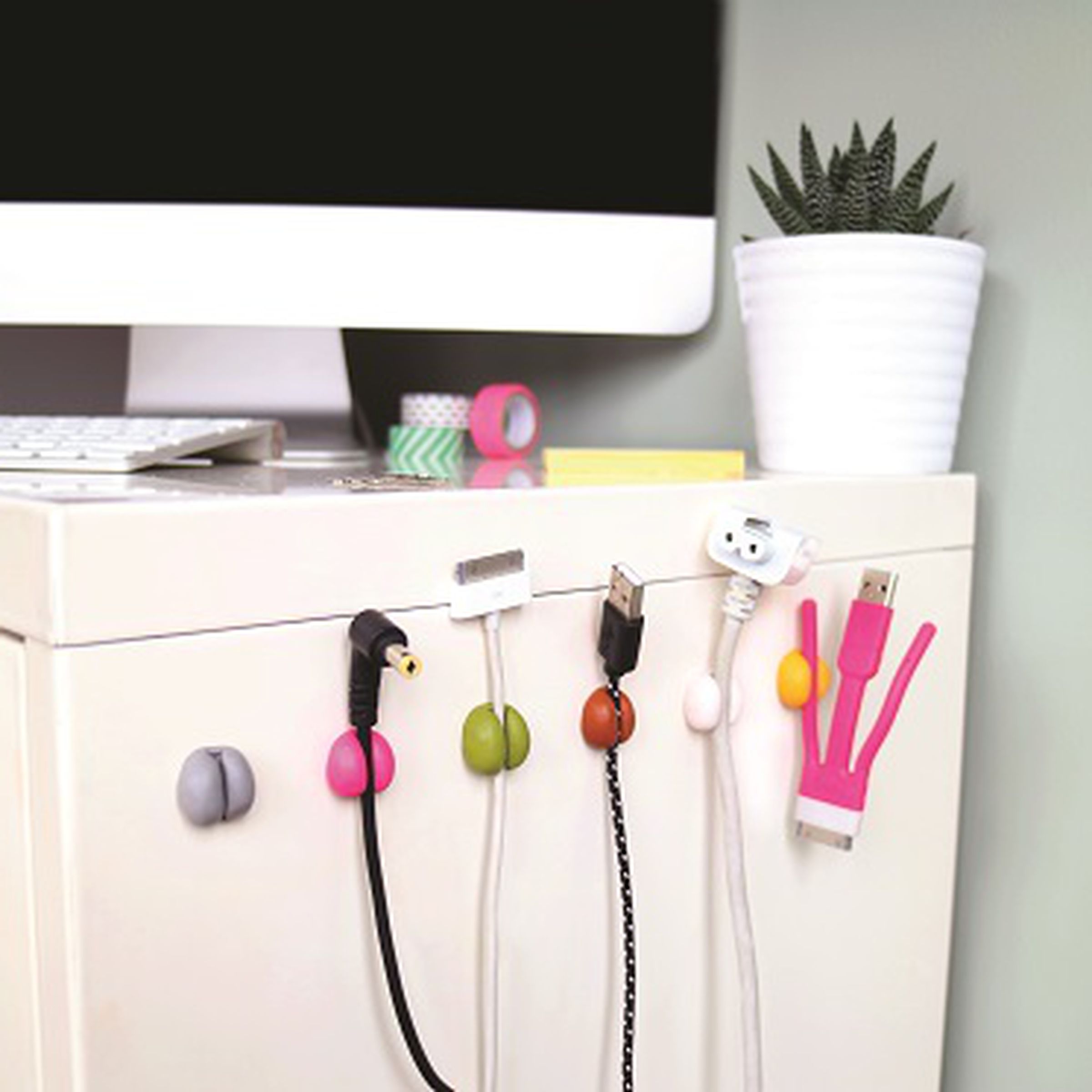 Round colorful cable holders stuck to the side of a desk.