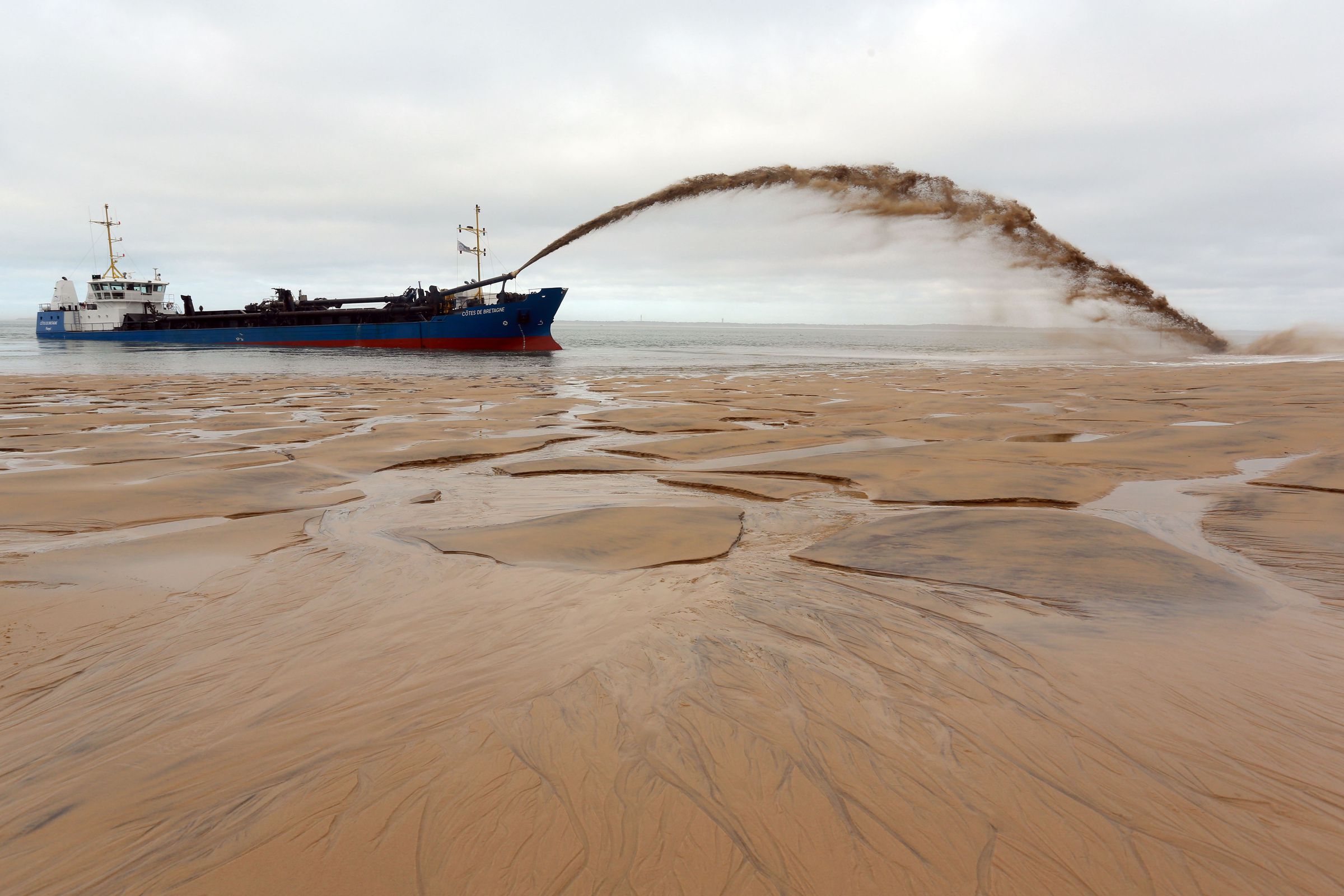 A boat sprays an arc of sandy water onto an empty beach.