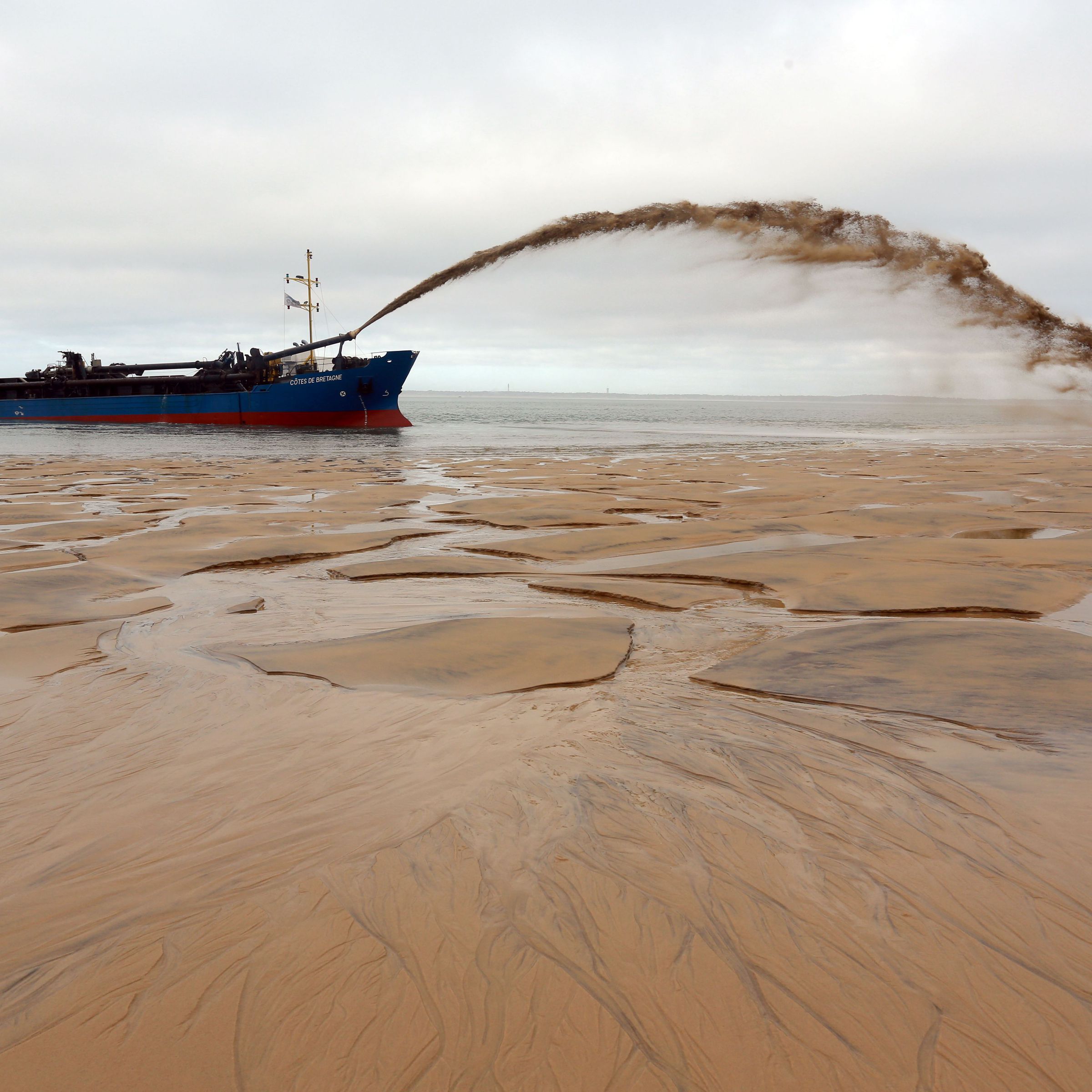 A boat sprays an arc of sandy water onto an empty beach.
