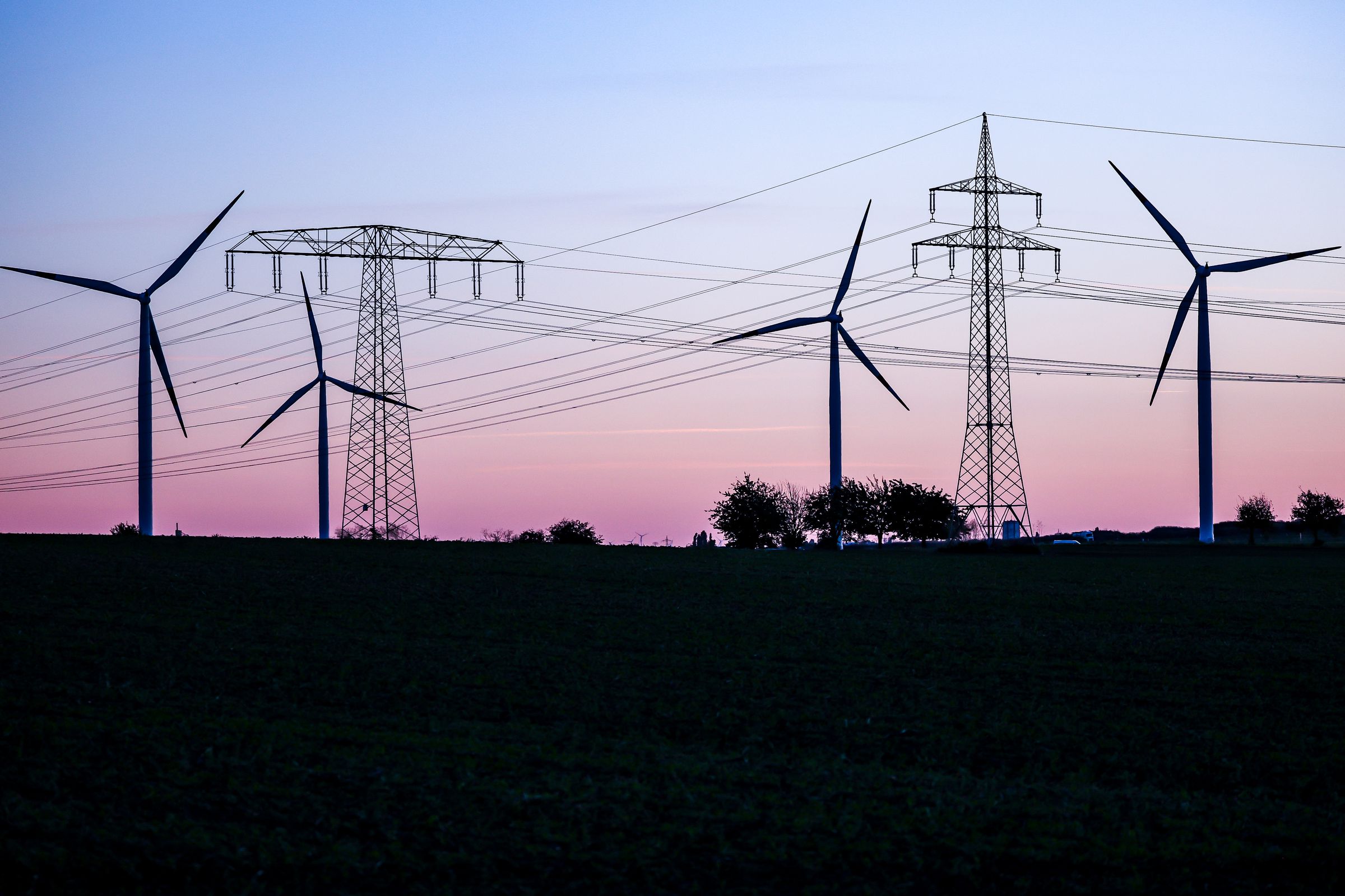 The silhouette of four wind turbines and transmission lines against a sunset.