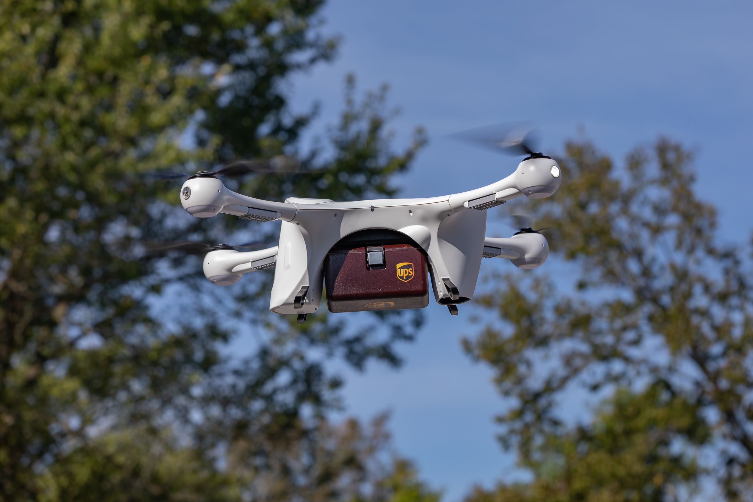 A UPS delivery drone flying in the sky against a tree.