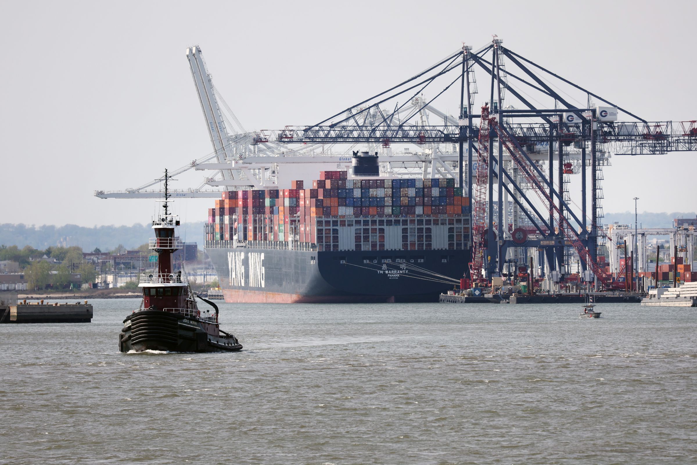 A cargo ship loaded with shipping containers sits on the water next to a port.