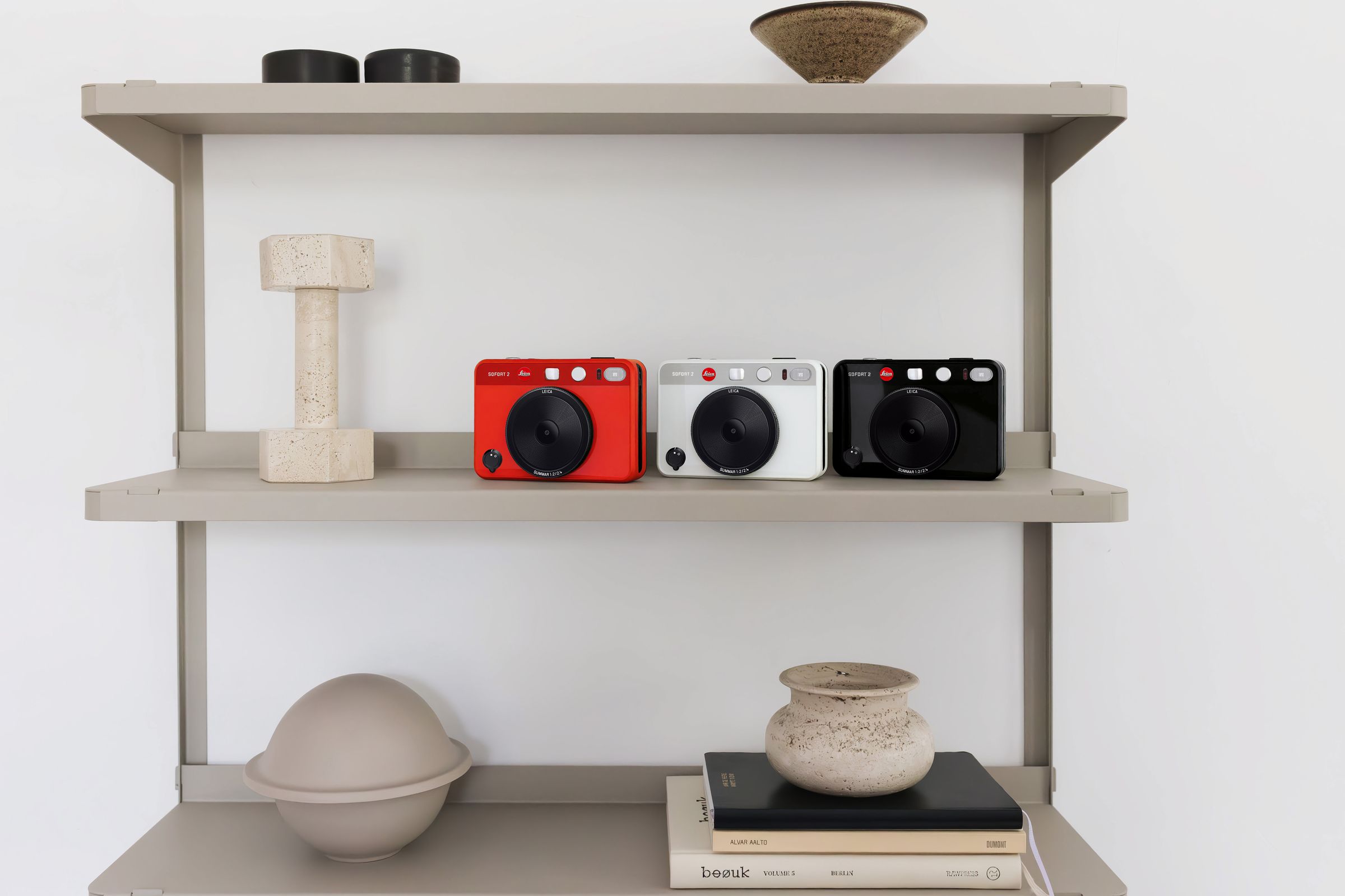 Red, black, and white versions of Leica Sofort 2 sitting on a shelf.