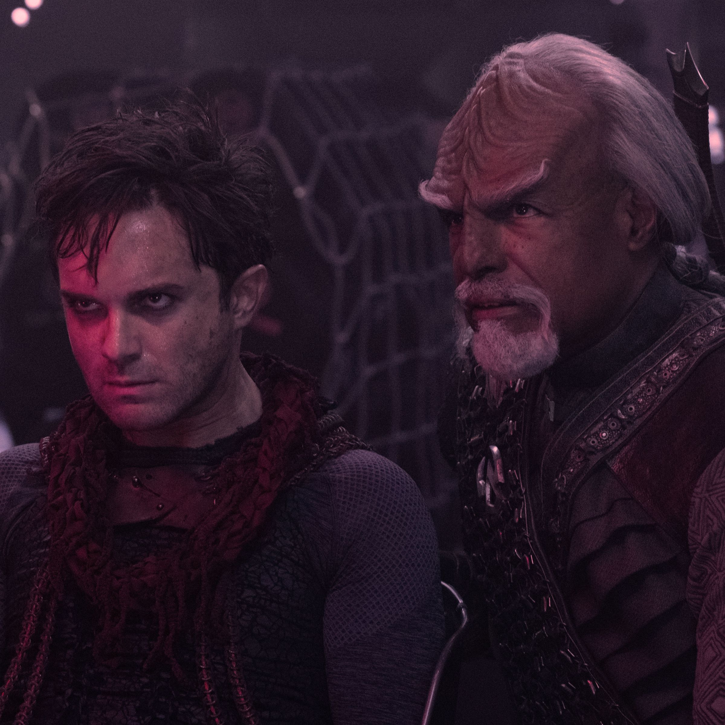 Two men look at something off-screen. One is a white man covered in grease; the other is Michael Dorn in Klingon makeup with white hair and large prominent cranial ridges.