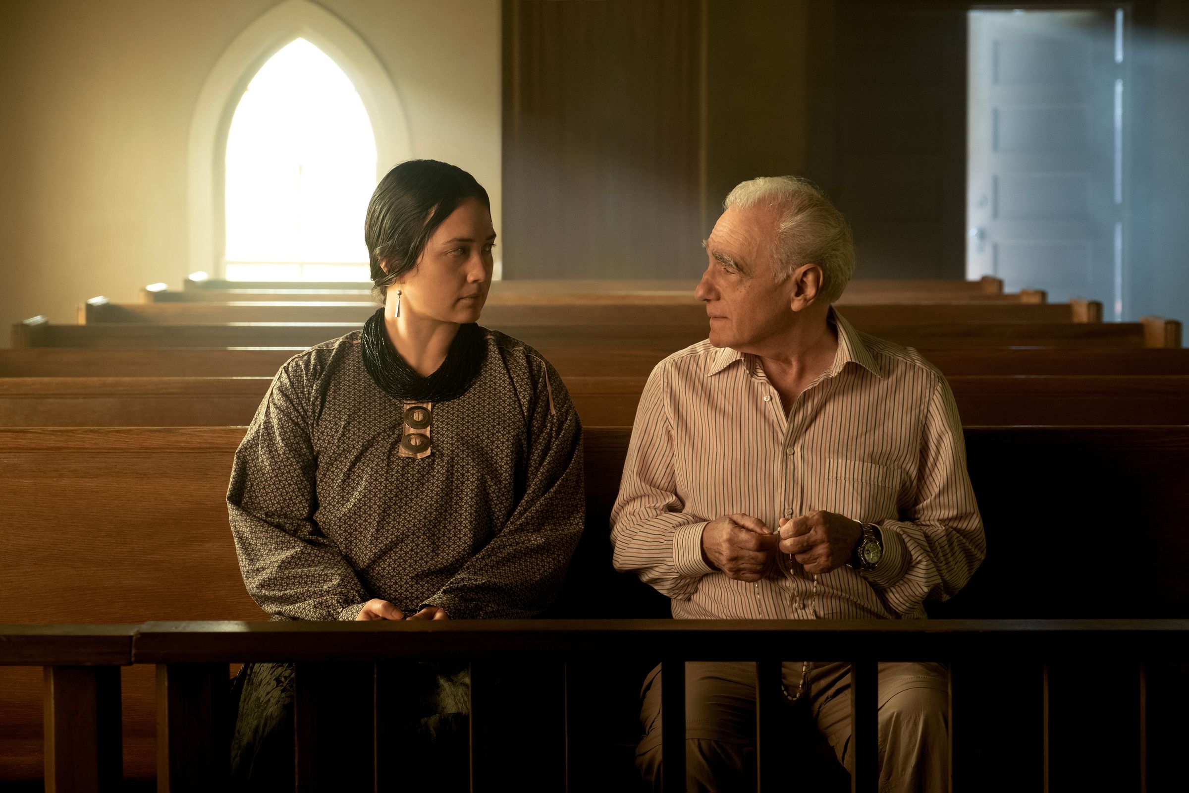 A woman in a gray dress and a man in a white shirt and slacks sitting together in the front of an empty church.