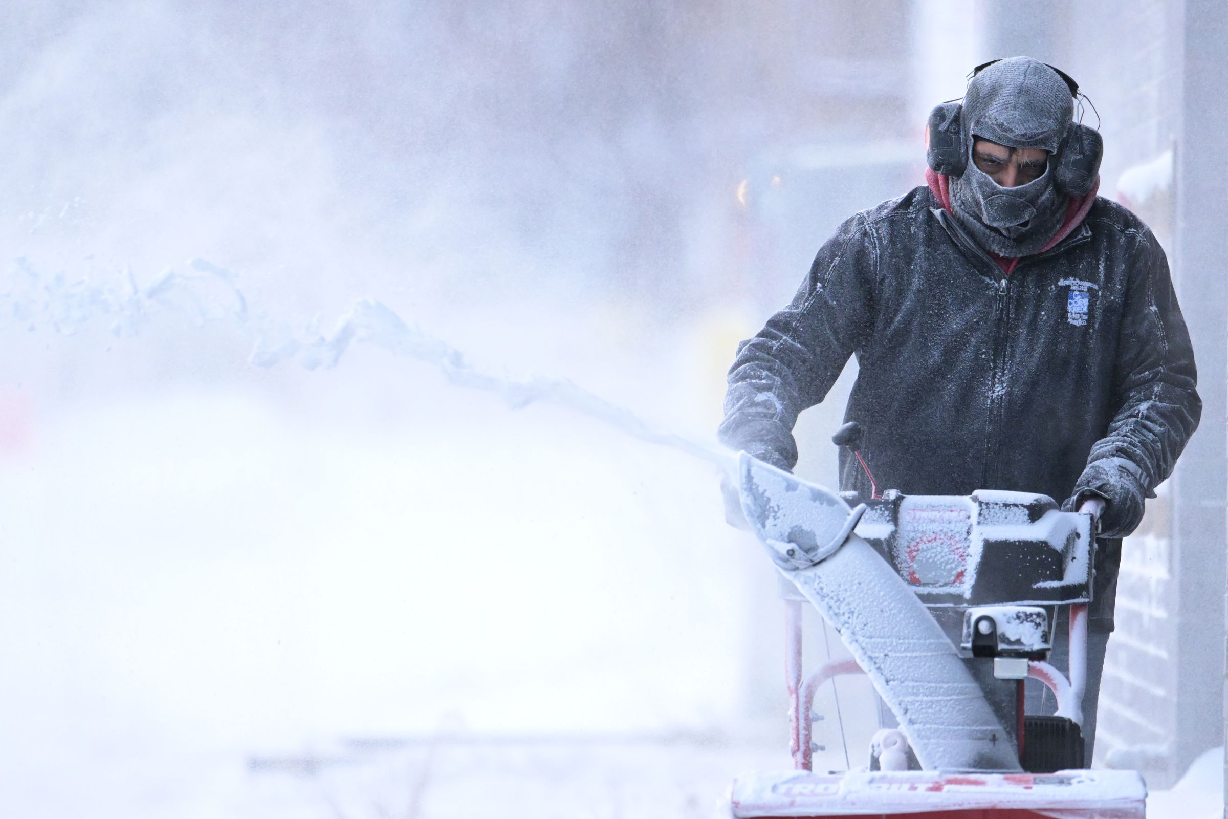 A bundled-up person pushes a snow blower