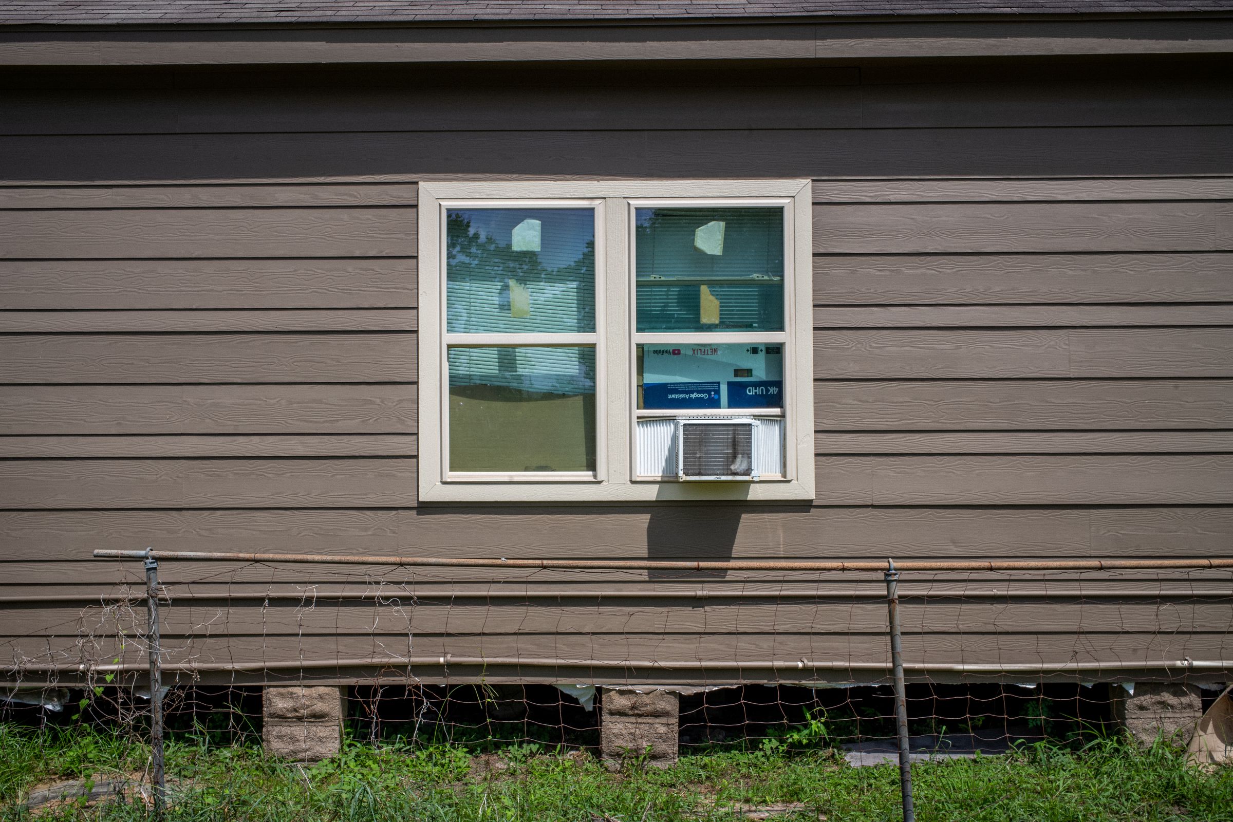 The side of a home with a small air conditioner sticking out of a window.