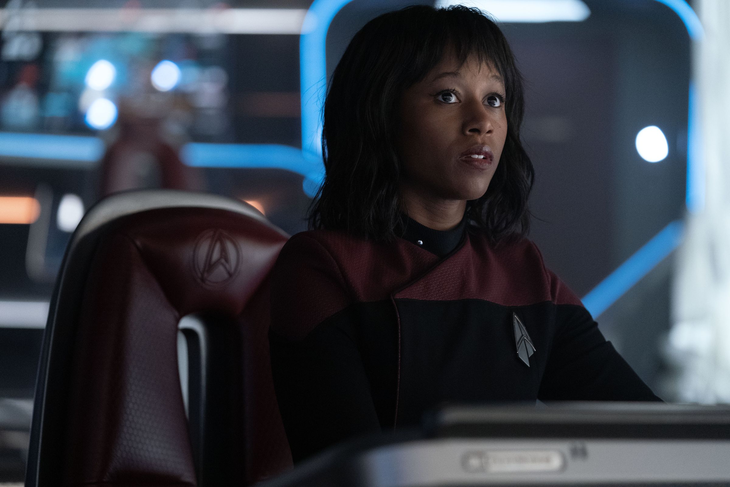 A young Black woman dressed in a Starfleet uniform stares at something off screen with concern.