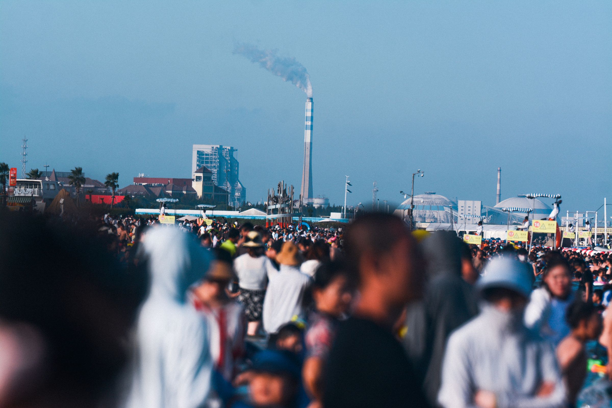 A smokestack bellows pollution behind a crowd of people at the beach.