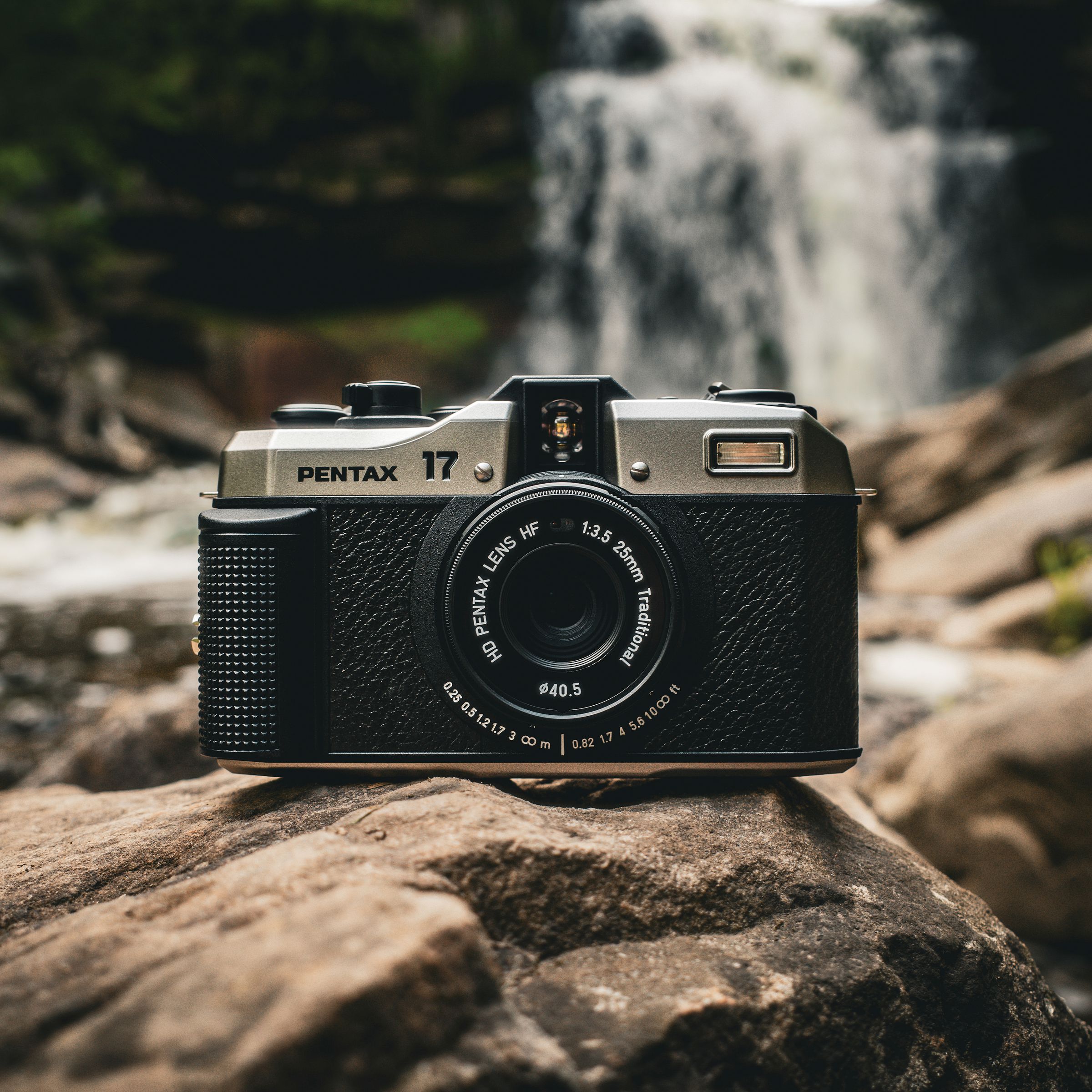 The Pentax 17 film camera resting on rocks in front of a waterfall.