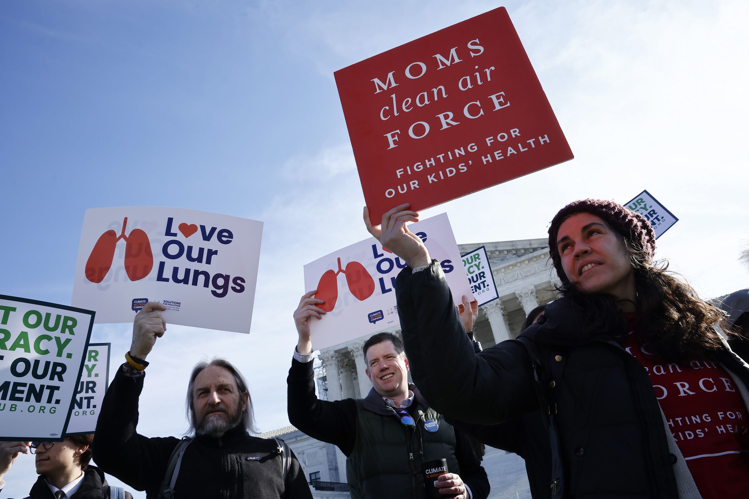 A group of protesters stand in front of the courthouse holding signs that say “Love our lungs” and “Moms Clean Air Task Force fighting for our kids’ health.”