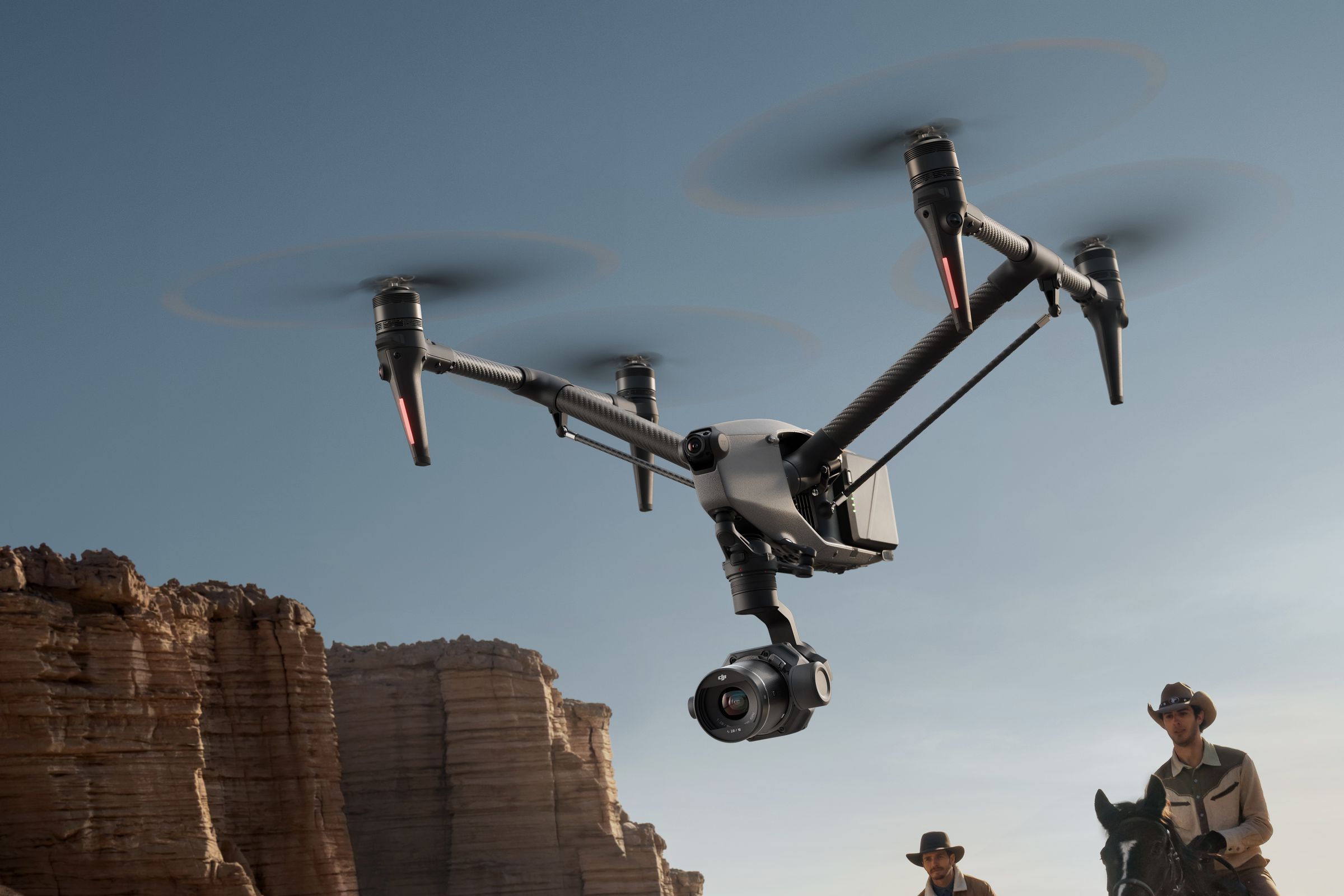 Inspire 3 drone flying low with cowboys on horses following it and cliffs in the background